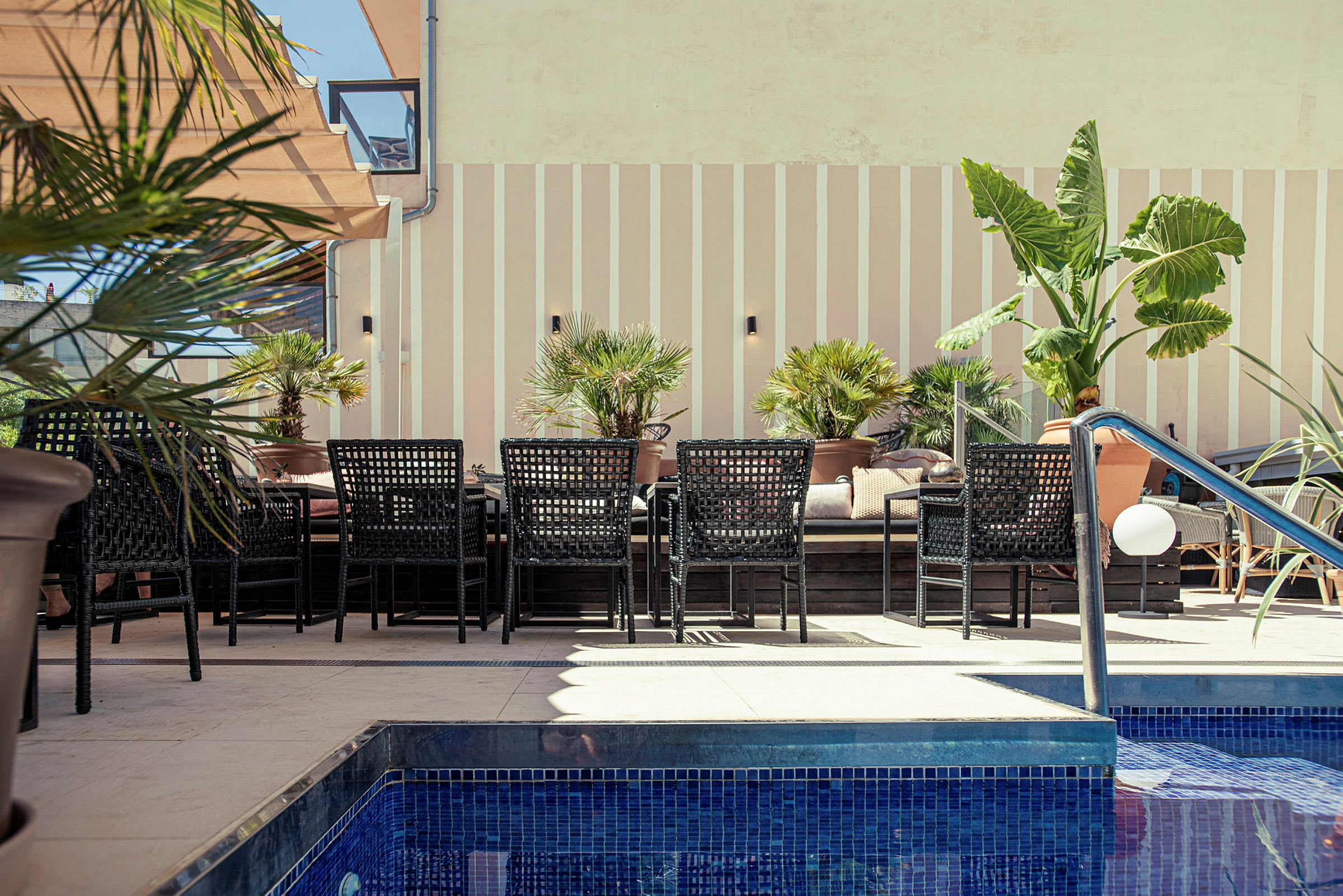 Utomhusområde med pool, bord och stolar bredvid planterade palmväxter. (AI-genererad text)