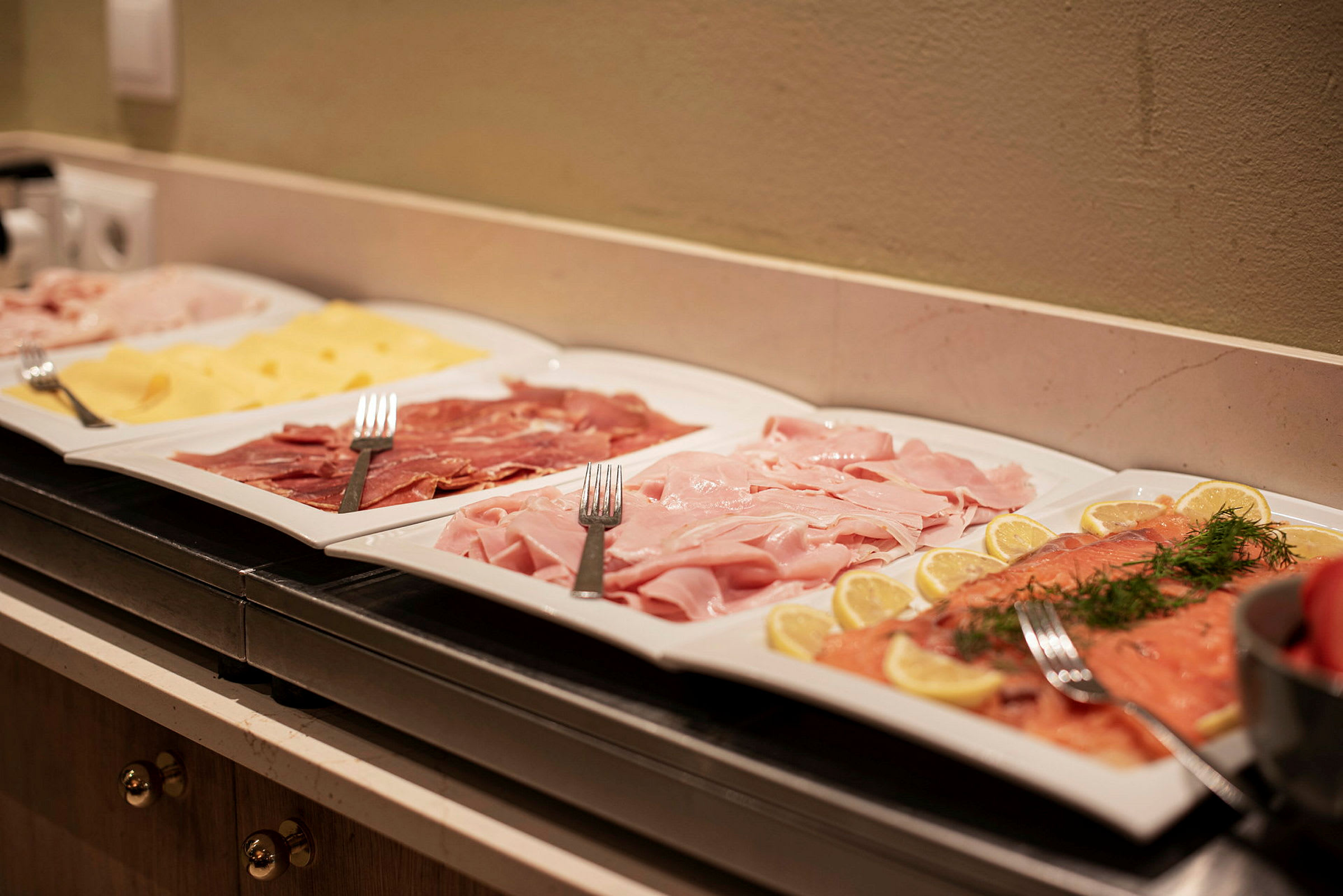 Fat med olika kallskuret och ost arrangerat på en buffé. (AI-genererad text)