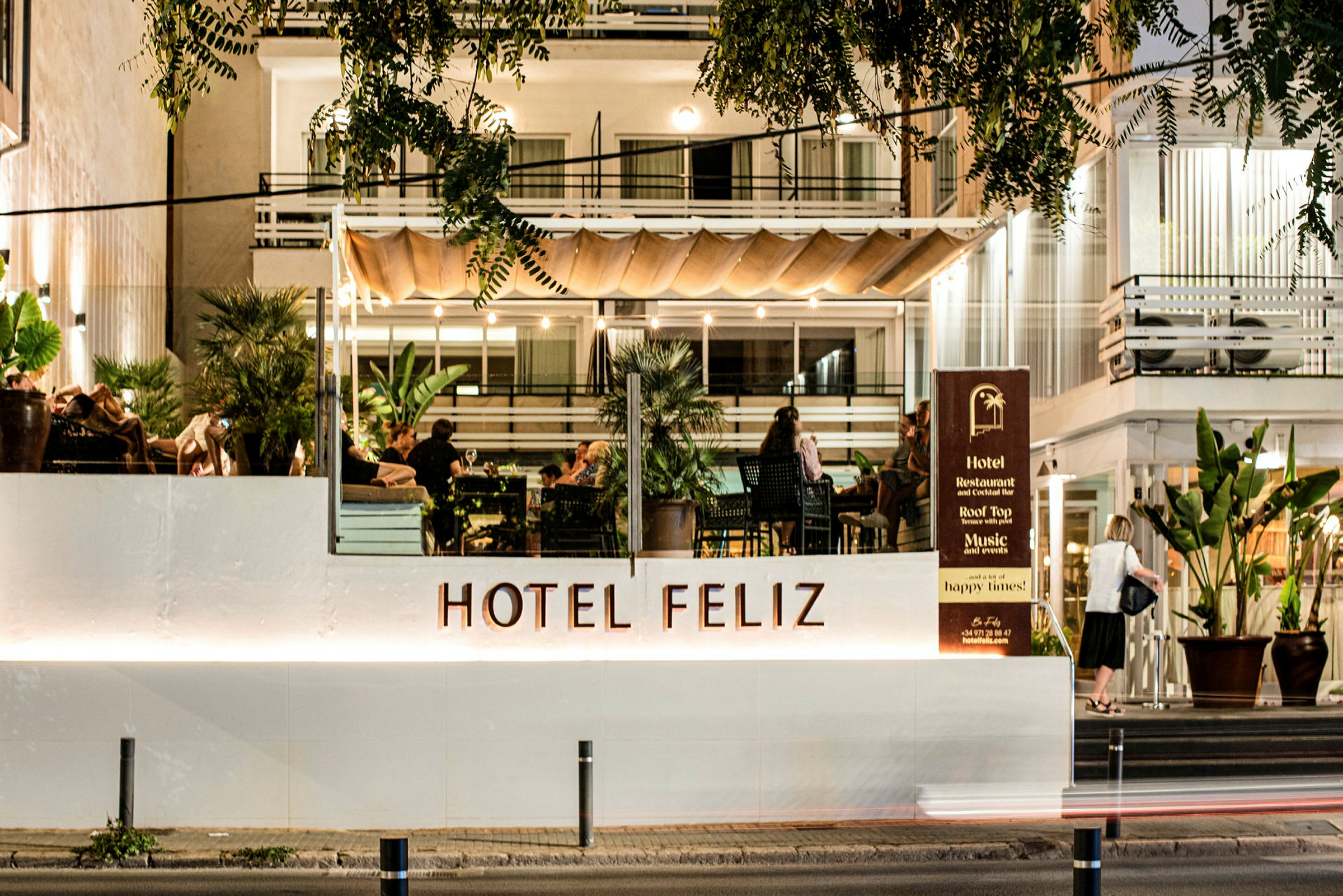 Hotell Feliz med upplyst fasad och terrass där människor sitter. (AI-genererad text)