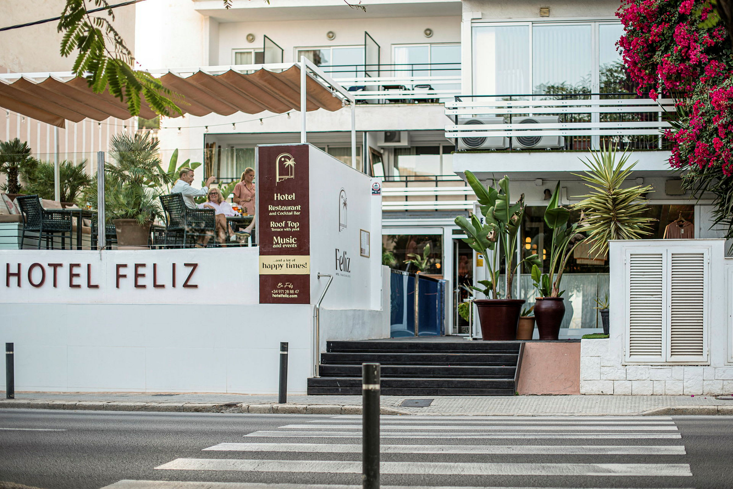 Hotel Feliz med uteservering och blommande växtlighet. (AI-genererad text)