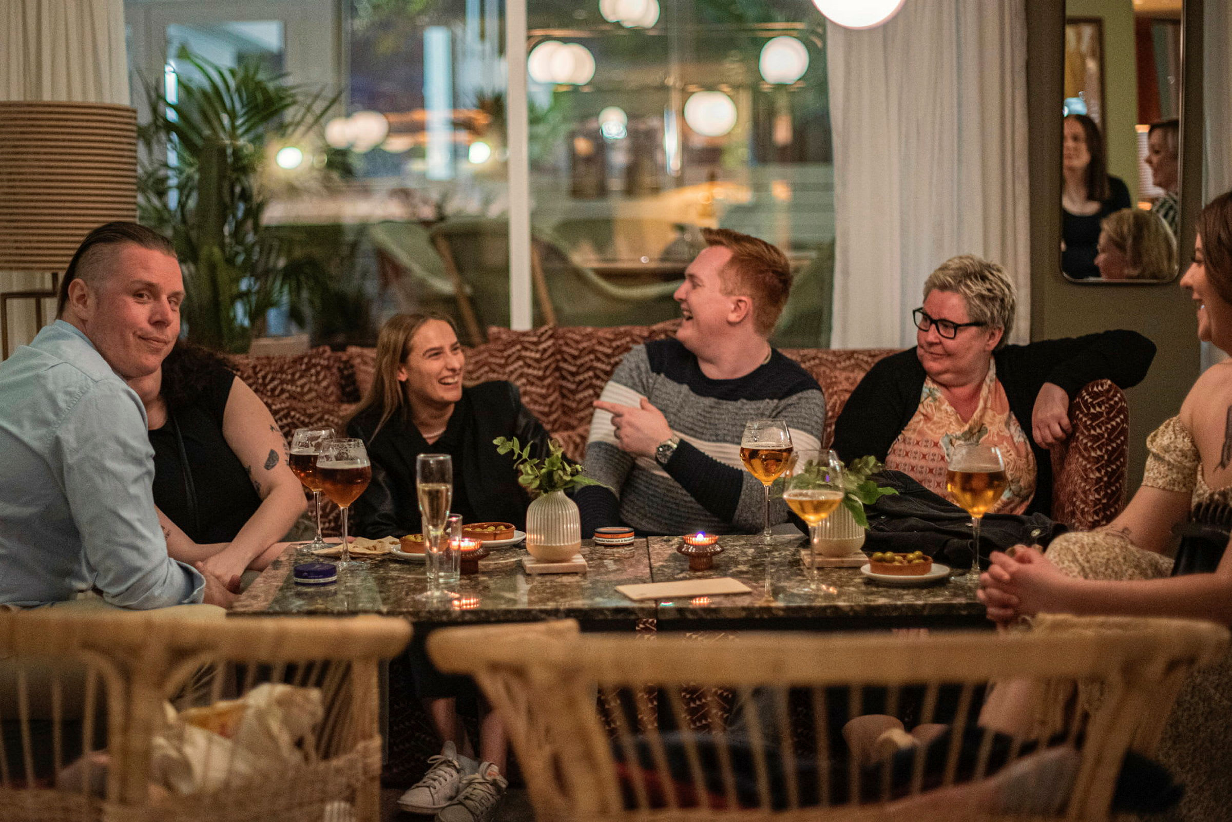 Människor sitter vid ett bord med drycker och tilltugg på en restaurang. (AI-genererad text)