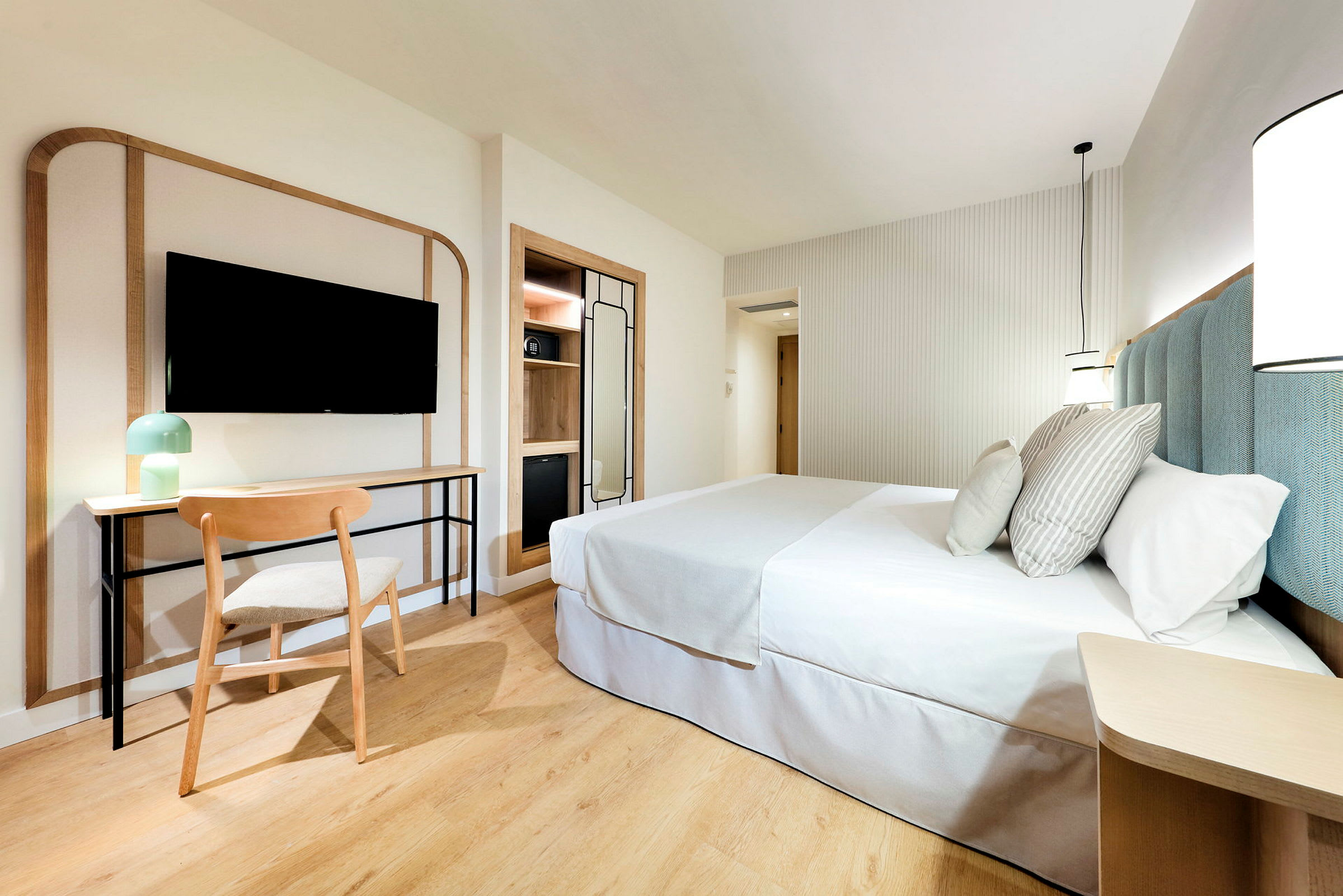 Ett modernt och ljust hotellrum med en dubbelsäng, skrivbord och stol, samt en väggmonterad TV. (AI-genererad text)