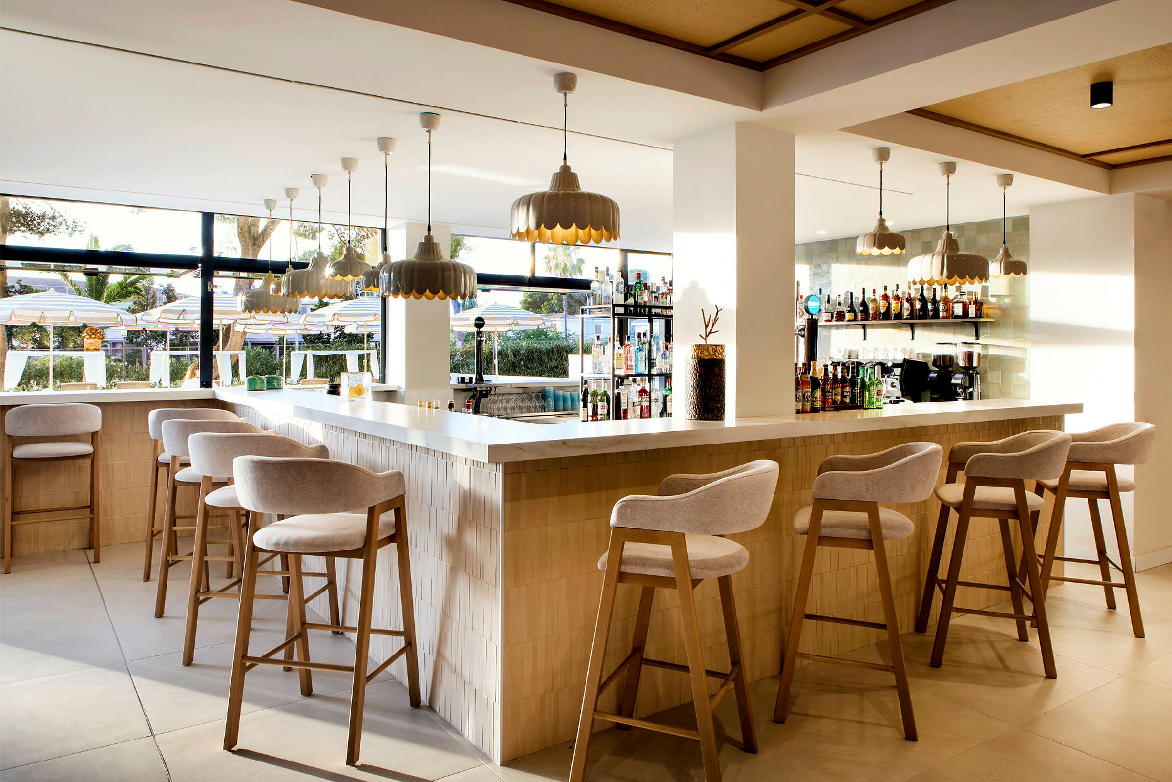 En modern bar med barstolar, hängande lampor och utsikt mot en utomhuspool. (AI-genererad text)