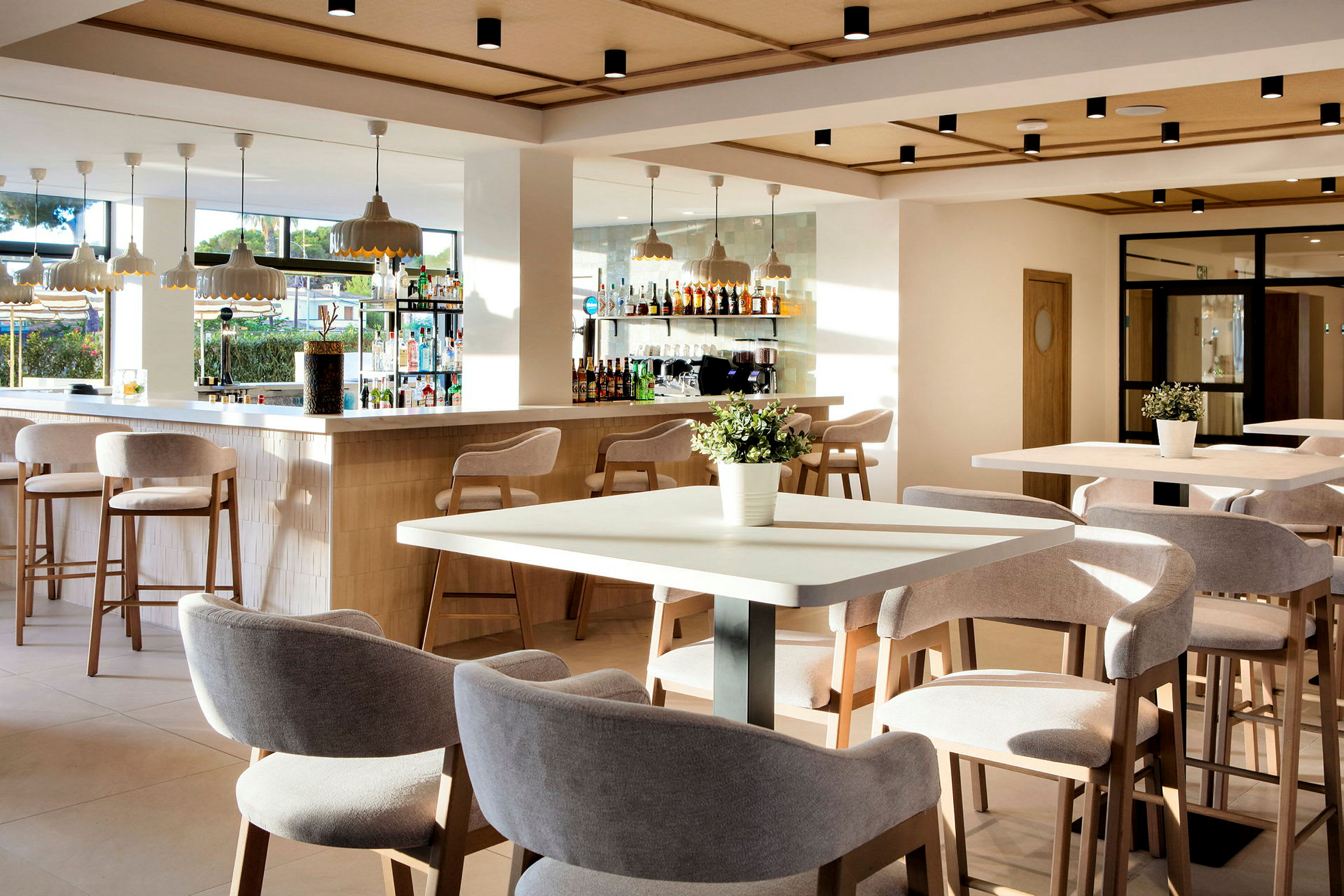En ljus och modern bar och restaurang med sittplatser vid bord och bar samt dekorativa detaljer som blomkrukor. (AI-genererad text)