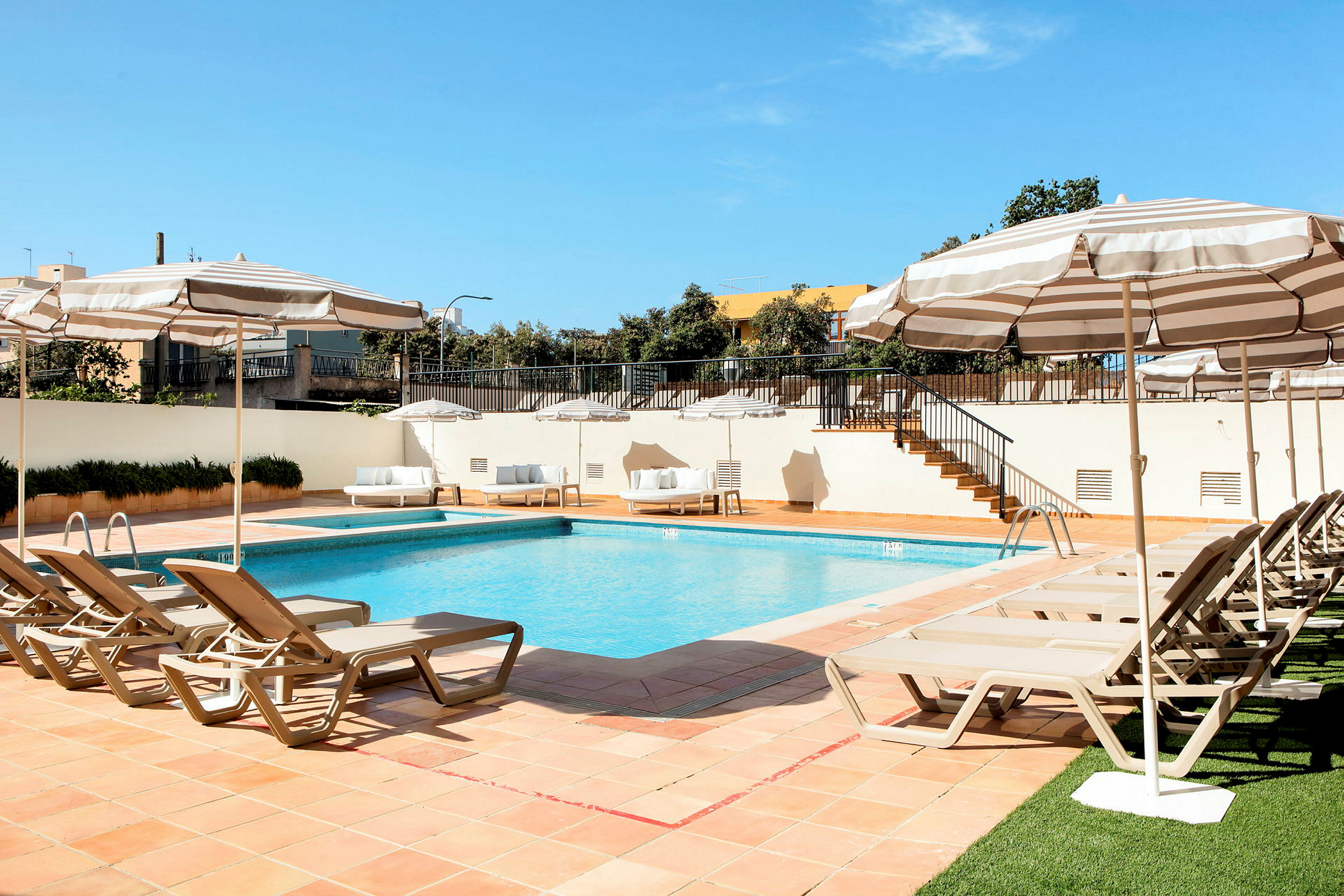 Bild på en pool omgiven av solstolar och parasoller med en blå himmel i bakgrunden. (AI-genererad text)