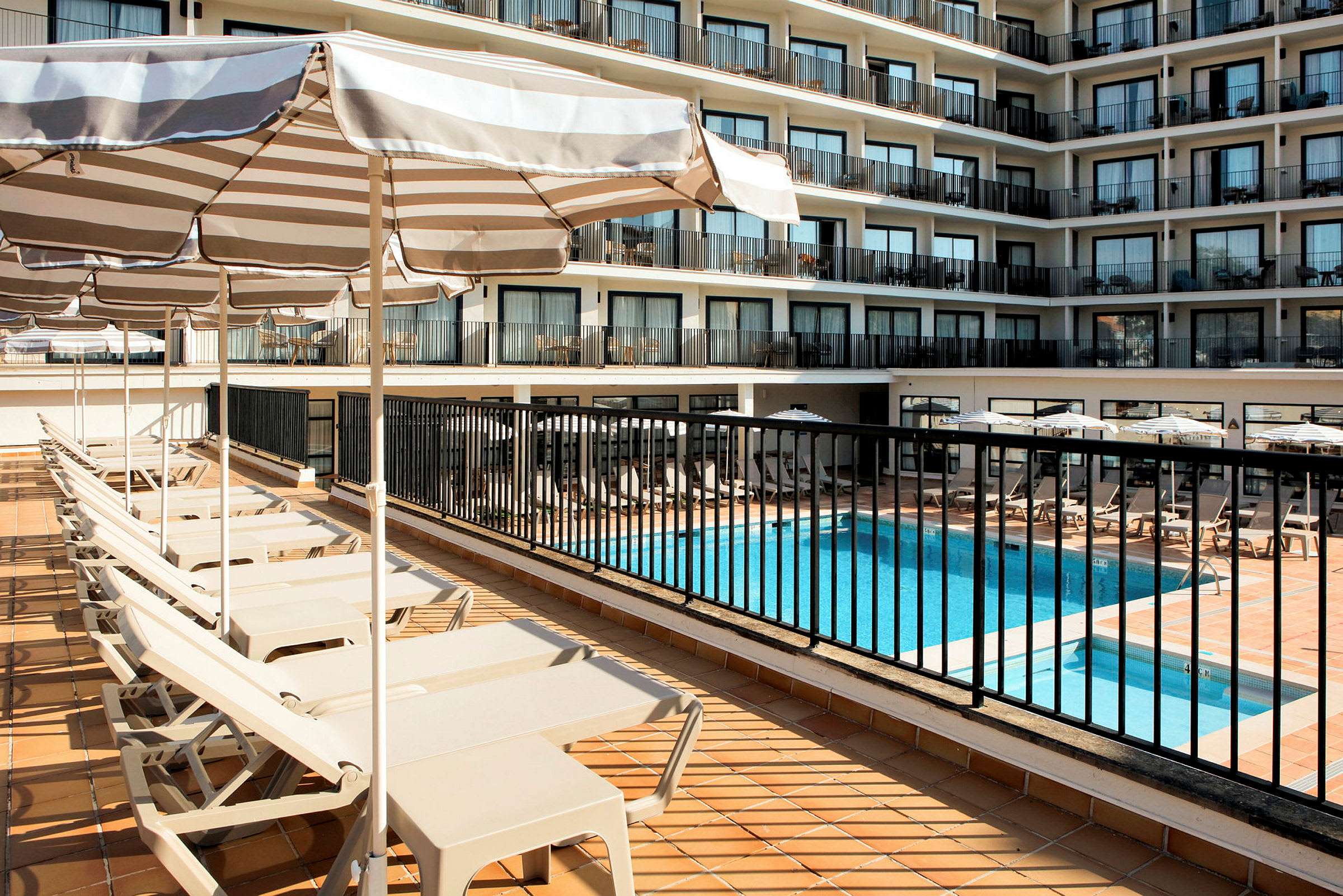 Utsikt över hotellpoolområde och solstolar med parasoller. (AI-genererad text)