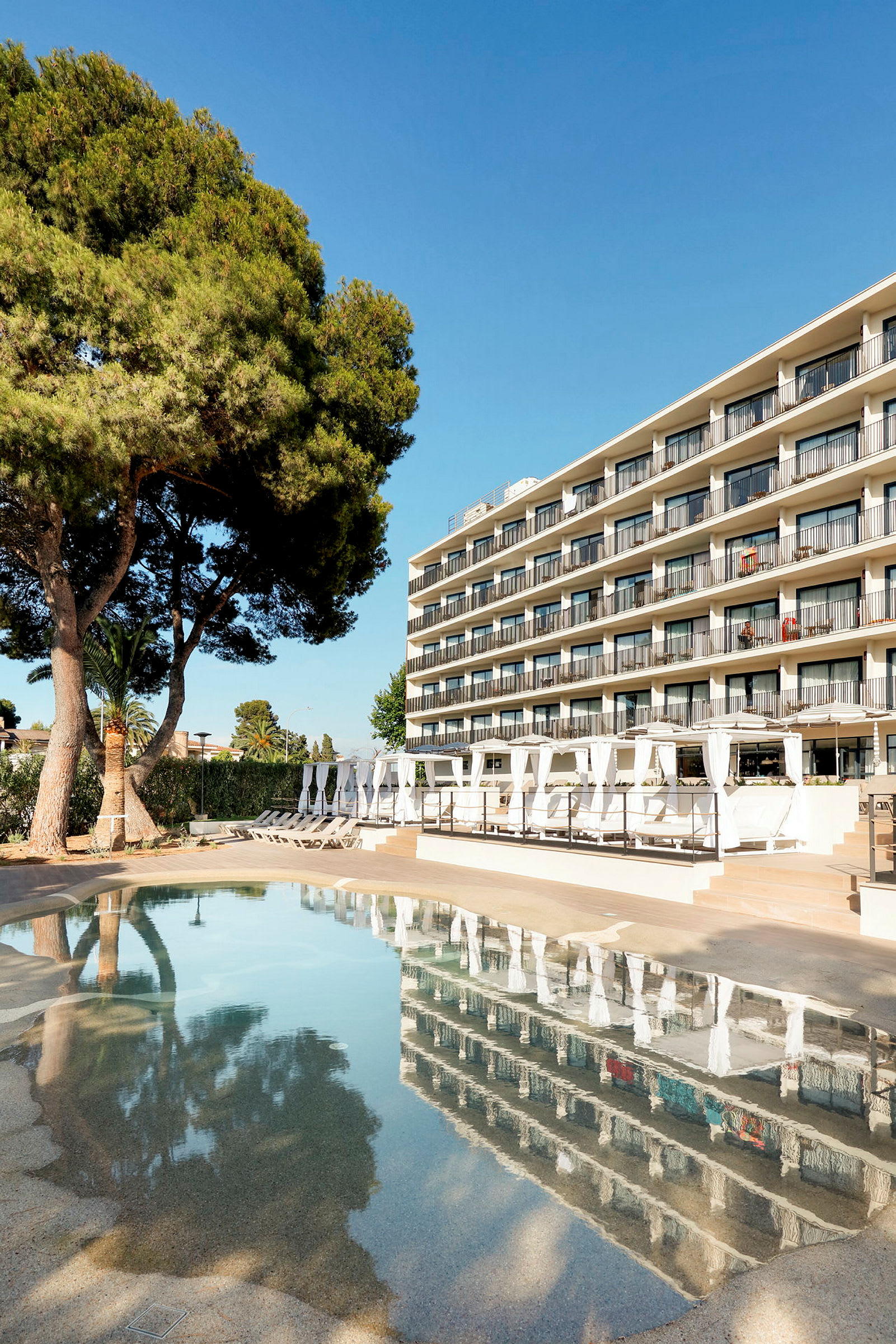 Ett hotell med flera balkonger vid en pool och träd i förgrunden. (AI-genererad text)