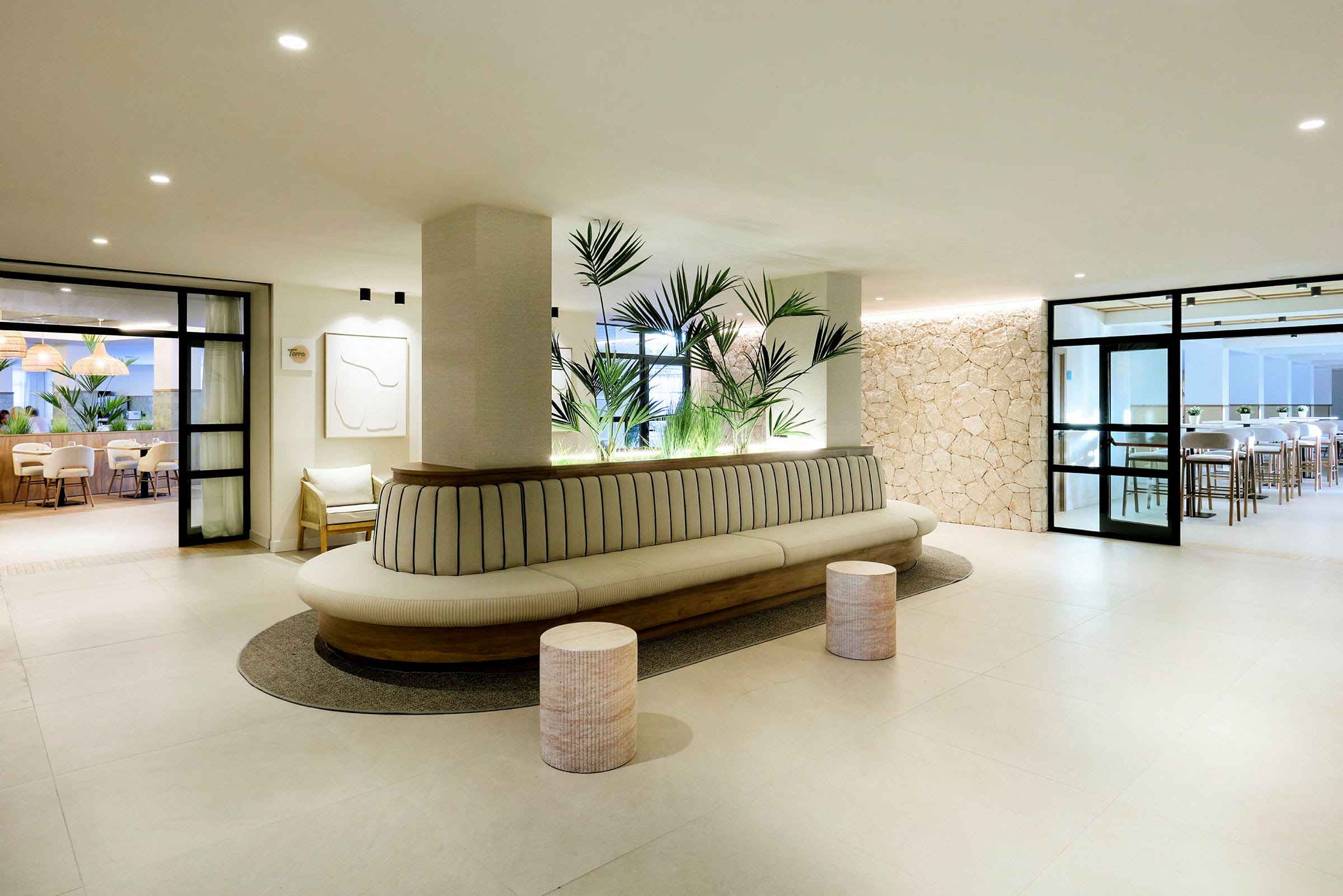 En modern lobby med ljus inredning, en lång soffa med plantor bakom och stolar samt bord syns i bakgrunden. (AI-genererad text)