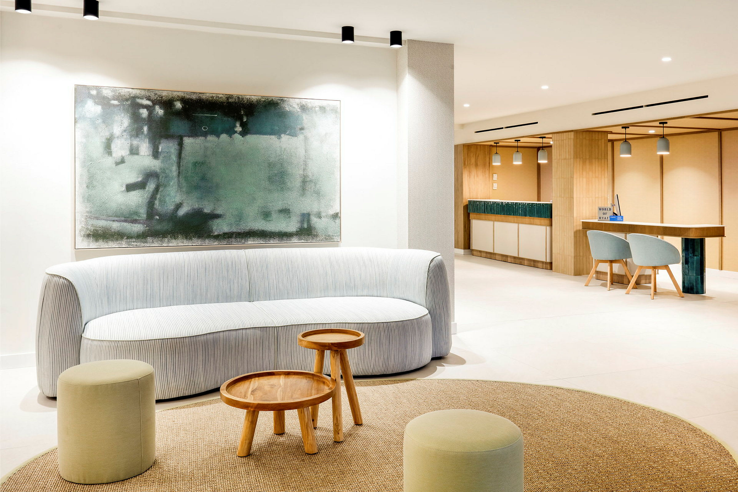 En ljus, modern lounge med en soffa, små träbord och pallar. En stor abstrakt tavla hänger på väggen bakom soffan. (AI-genererad text)