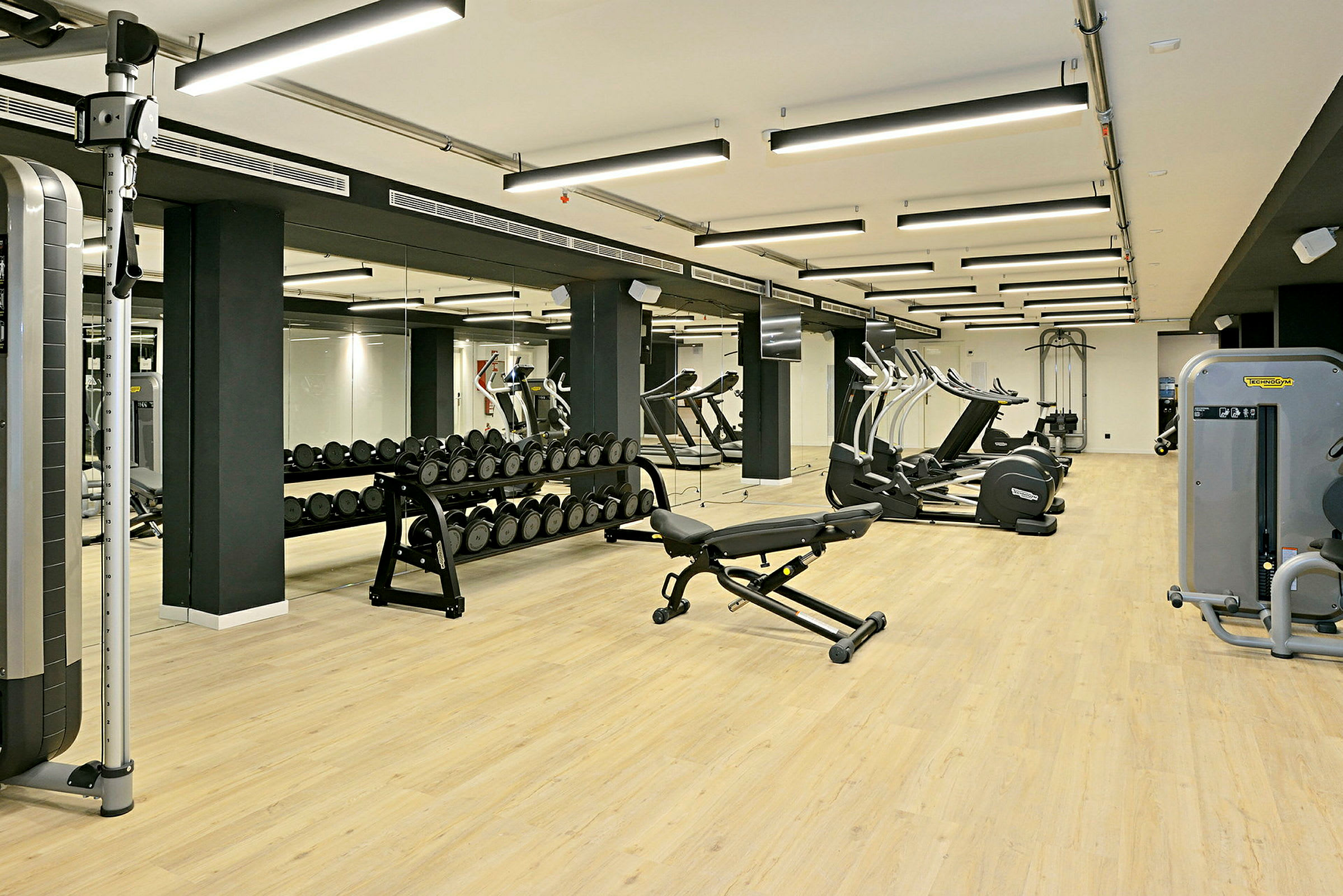 Ett gym med träningsutrustning inklusive vikter, bänkar och konditionsmaskiner. (AI-genererad text)