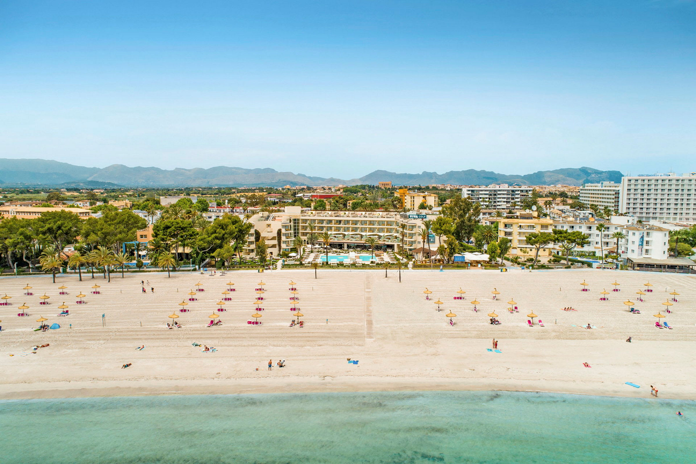 Strand med solsängar och parasoller, hotell samt stadssiluett i bakgrunden. (AI-genererad text)