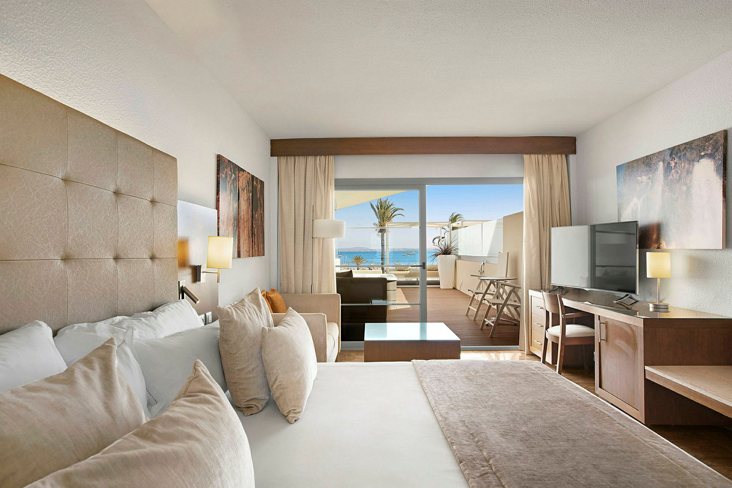 Hotellrum med säng, skrivbord, TV och en terrass med havsutsikt. (AI-genererad text)