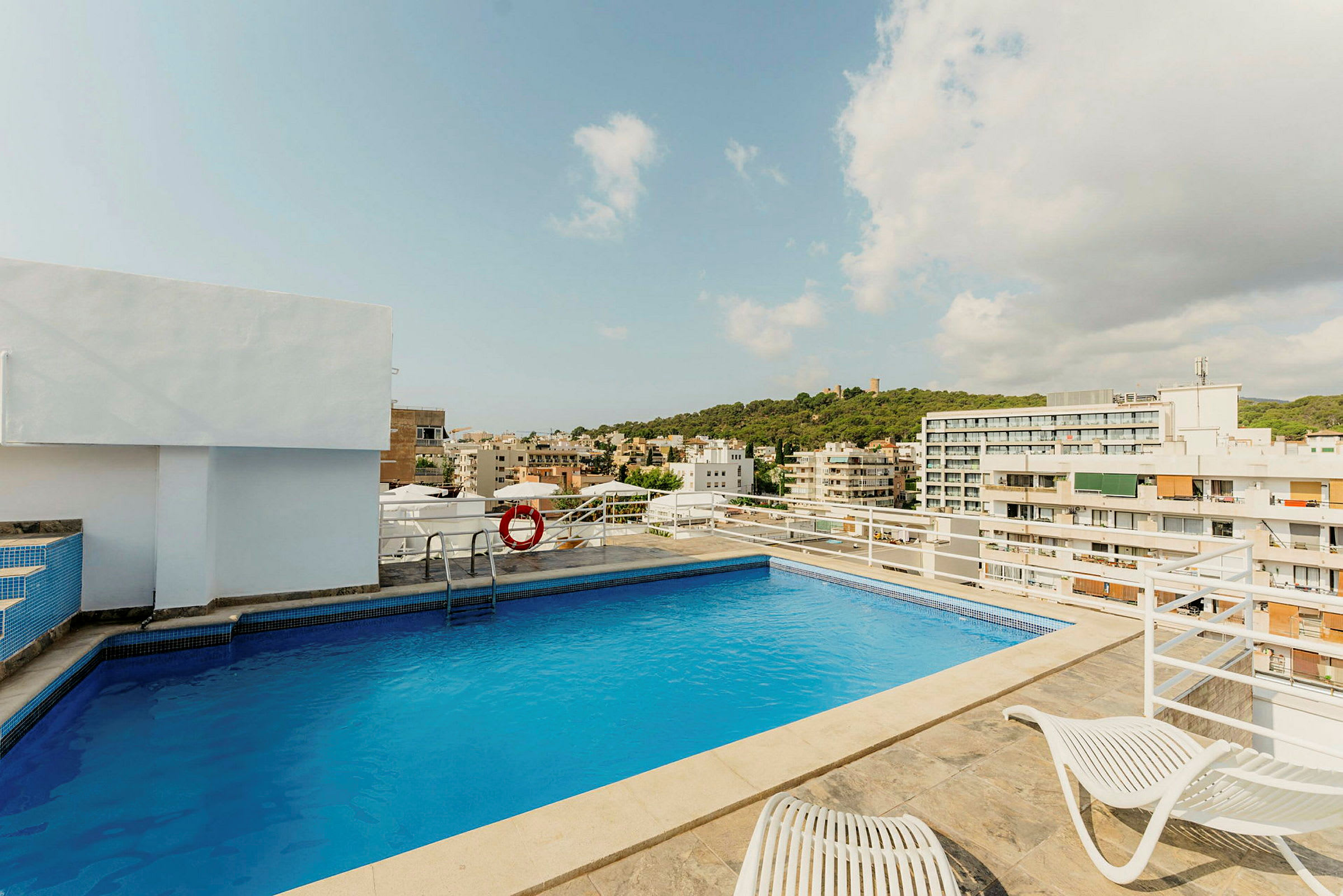 En takterrass med en pool, solstolar och utsikt över staden omgiven av byggnader och grönska. (AI-genererad text)