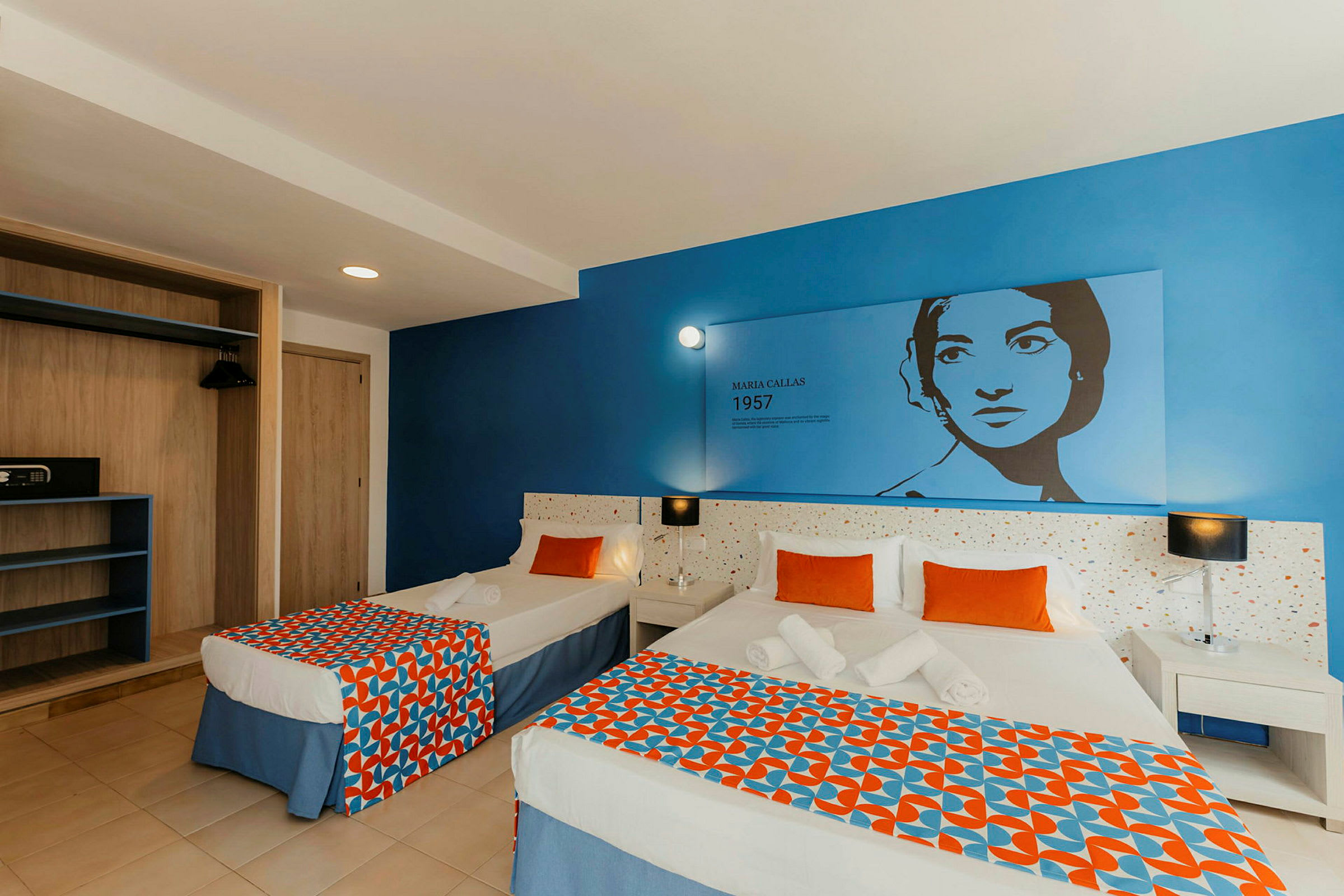 Ett hotellrum med två sängar, en blå vägg med dekor och en klädförvaring. (AI-genererad text)