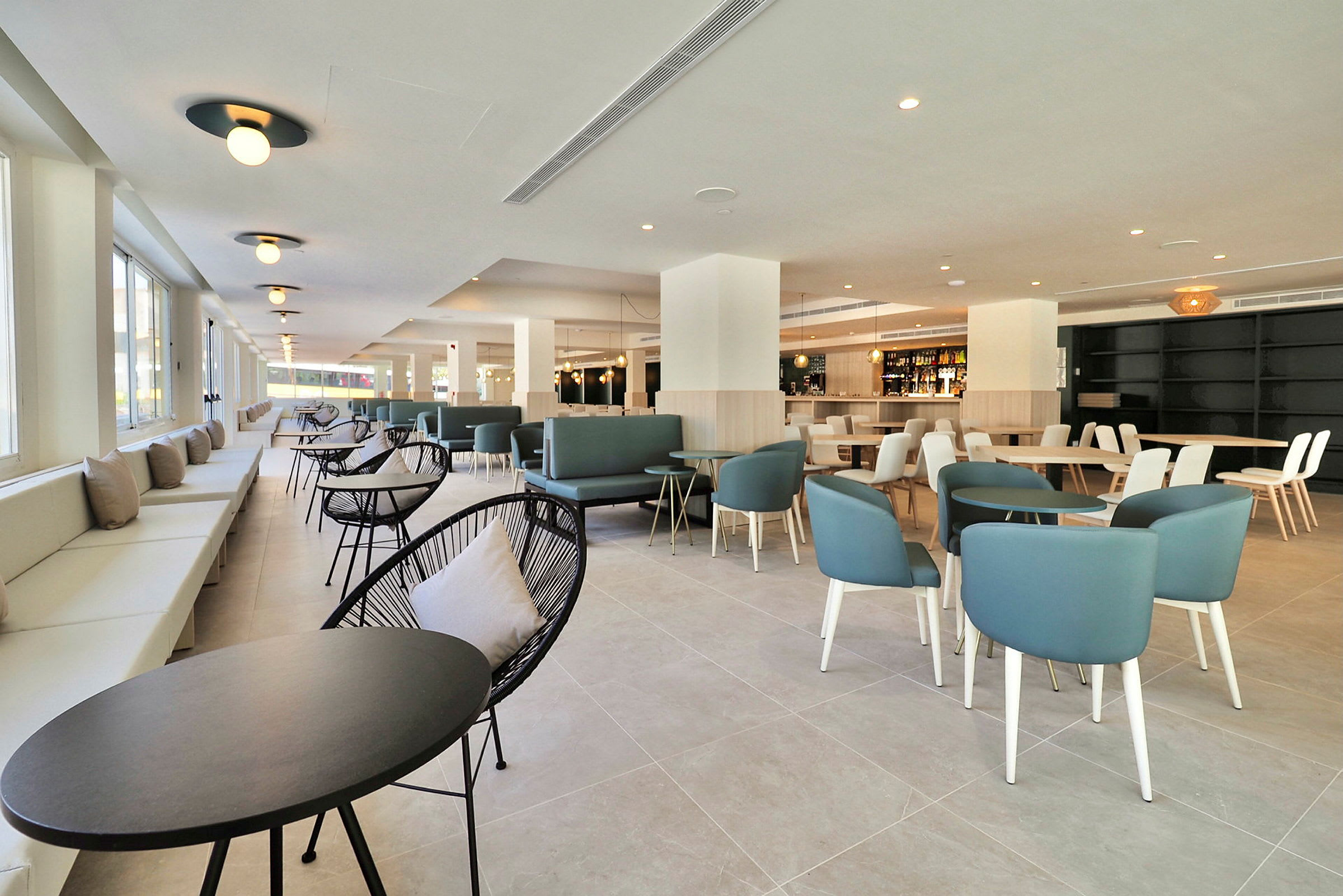 Bild av en modern och rymlig inomhuslounge eller restaurang, med bord och stolar, samt stora fönster som släpper in dagsljus. (AI-genererad text)