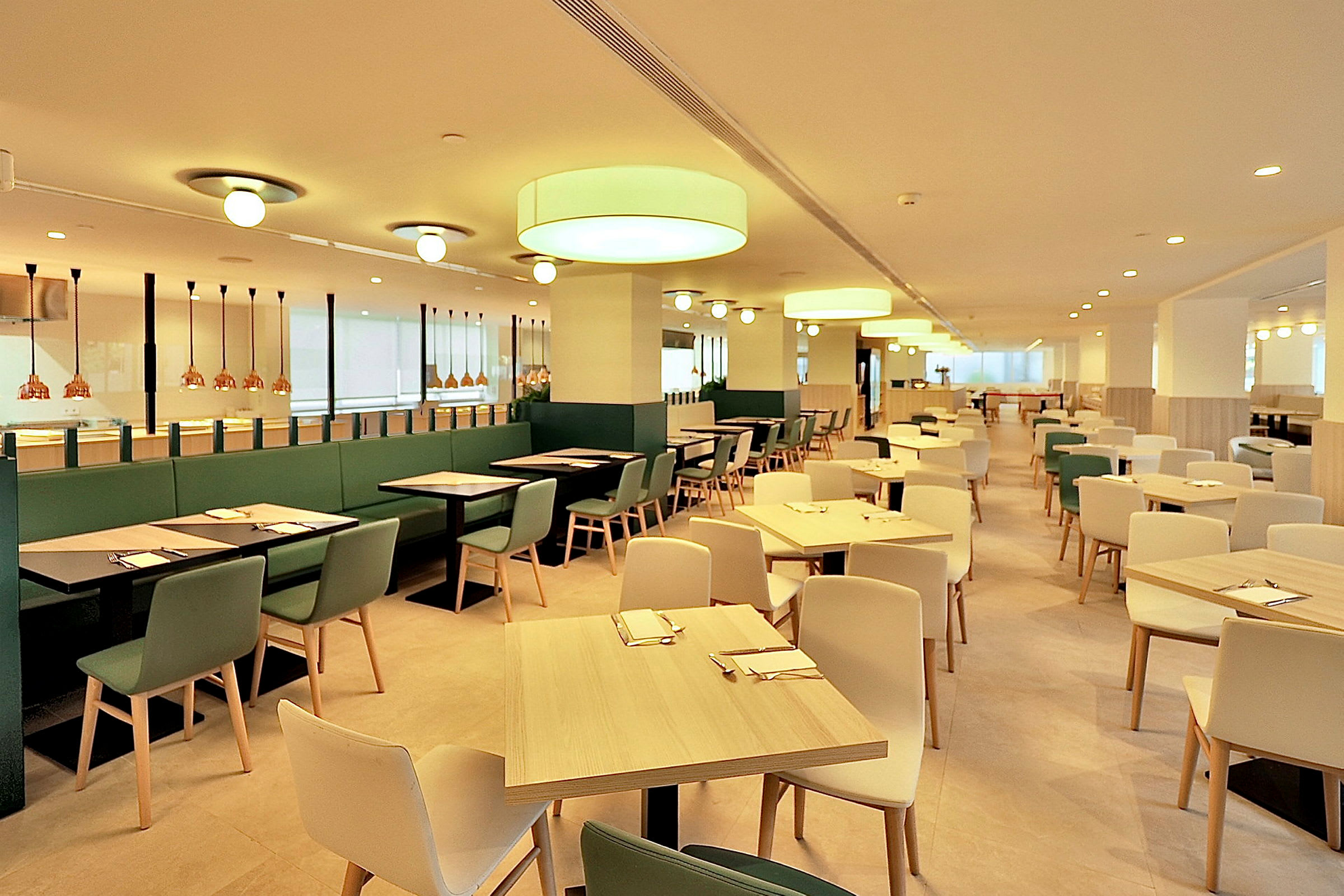 En ljus och rymlig restaurang med moderna möbler och belysning. Bord och stolar är arrangerade i jämna rader. (AI-genererad text)