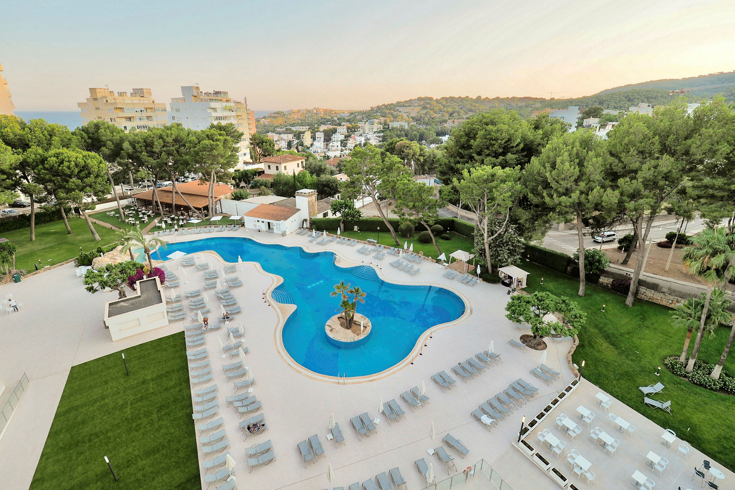 Bild av en hotellpool med solstolar, bord och grönska runt omkring. (AI-genererad text)