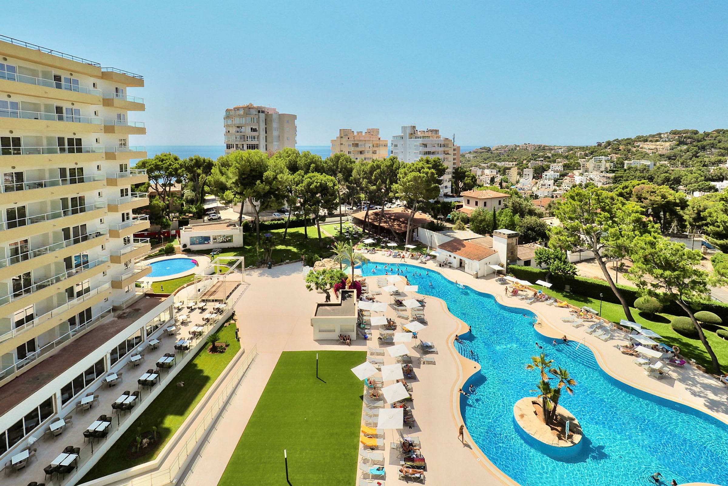 En hotellbyggnad bredvid en pool med solstolar och parasoller samt omgivande vegetation och utsikt över en stad. (AI-genererad text)