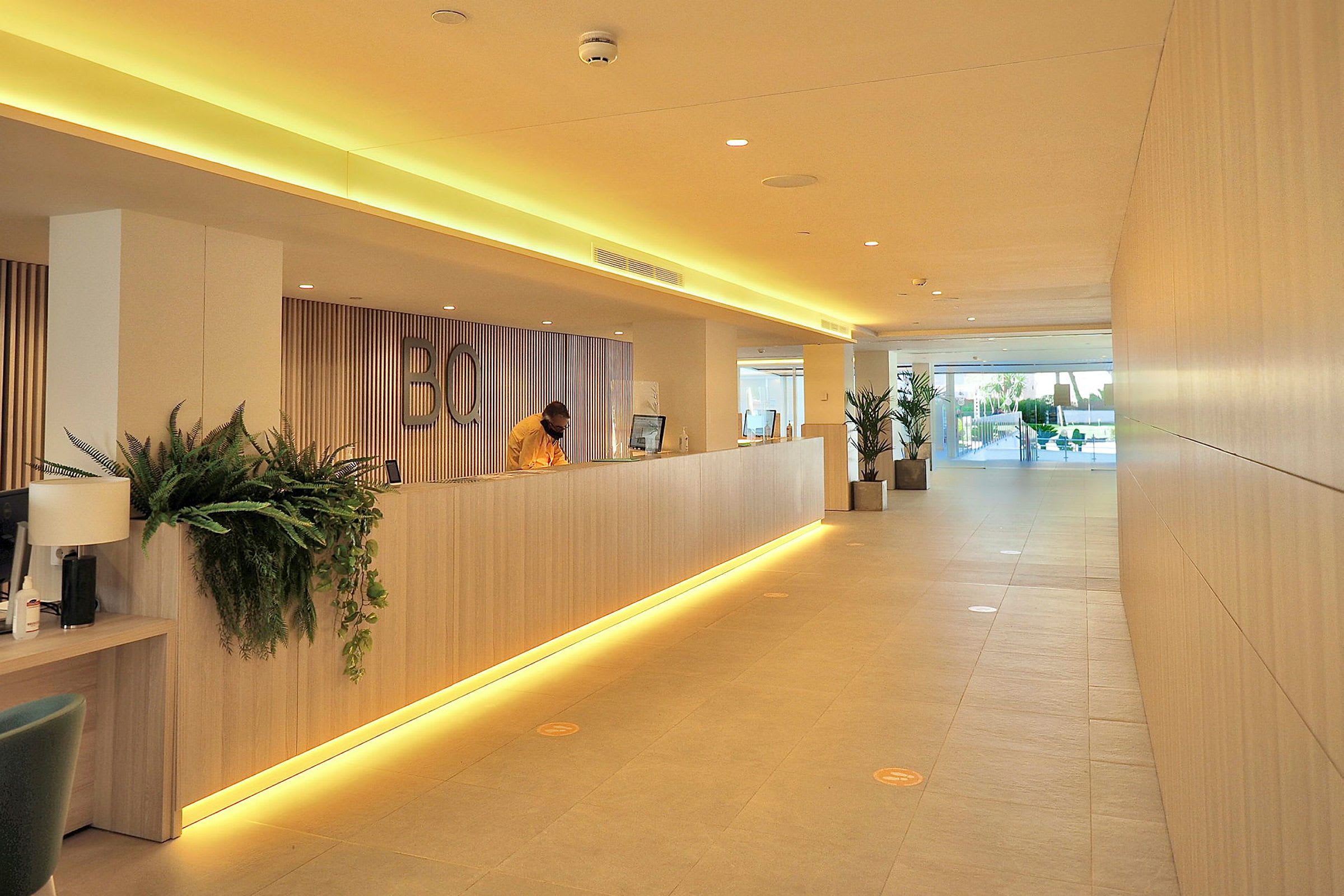 Ljus hotellreception med en lång trädisk, moderna detaljer och växtdekorationer. (AI-genererad text)