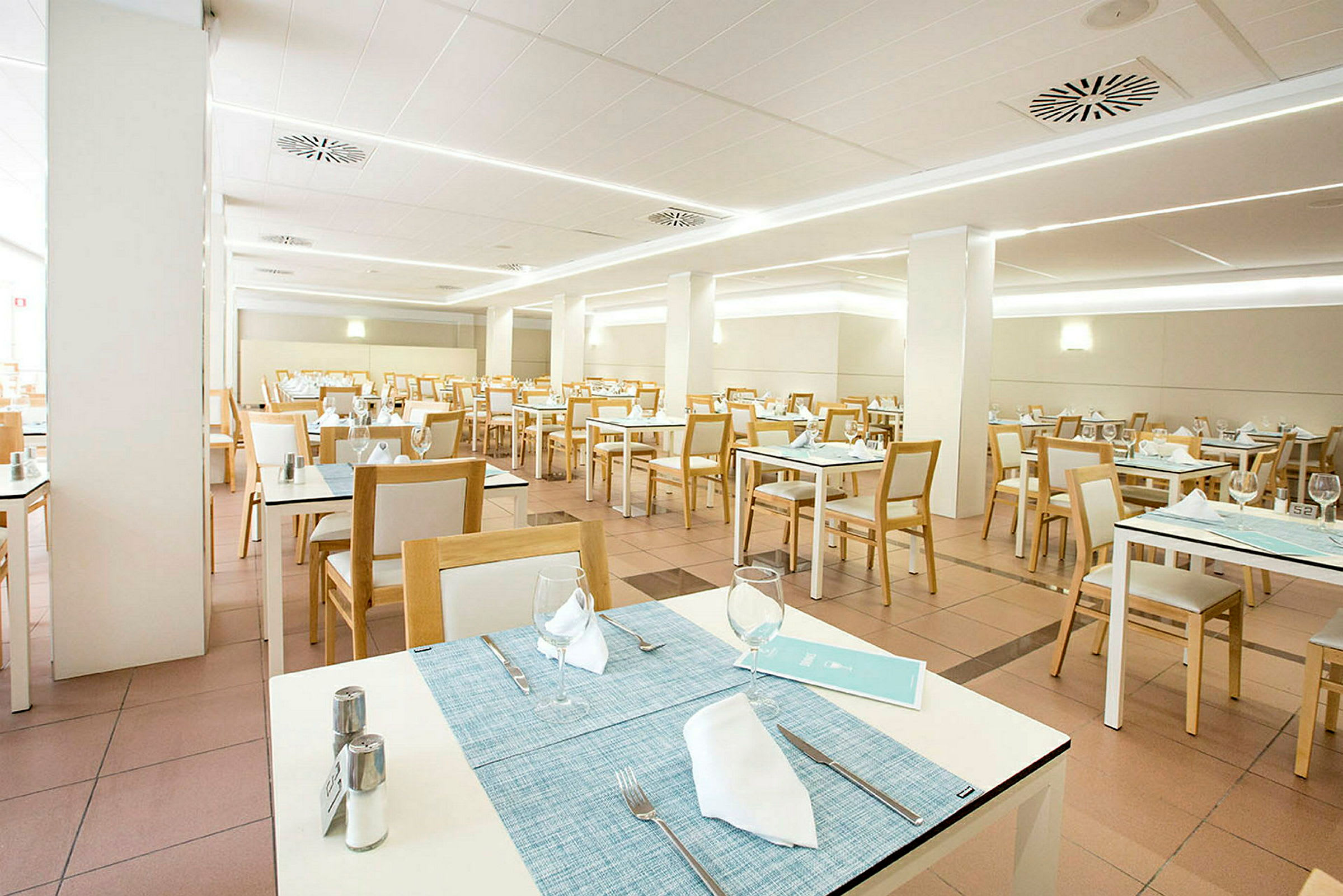 En ljus och modern restaurang med vita bord och trästolar, uppdukad för matgäster. (AI-genererad text)