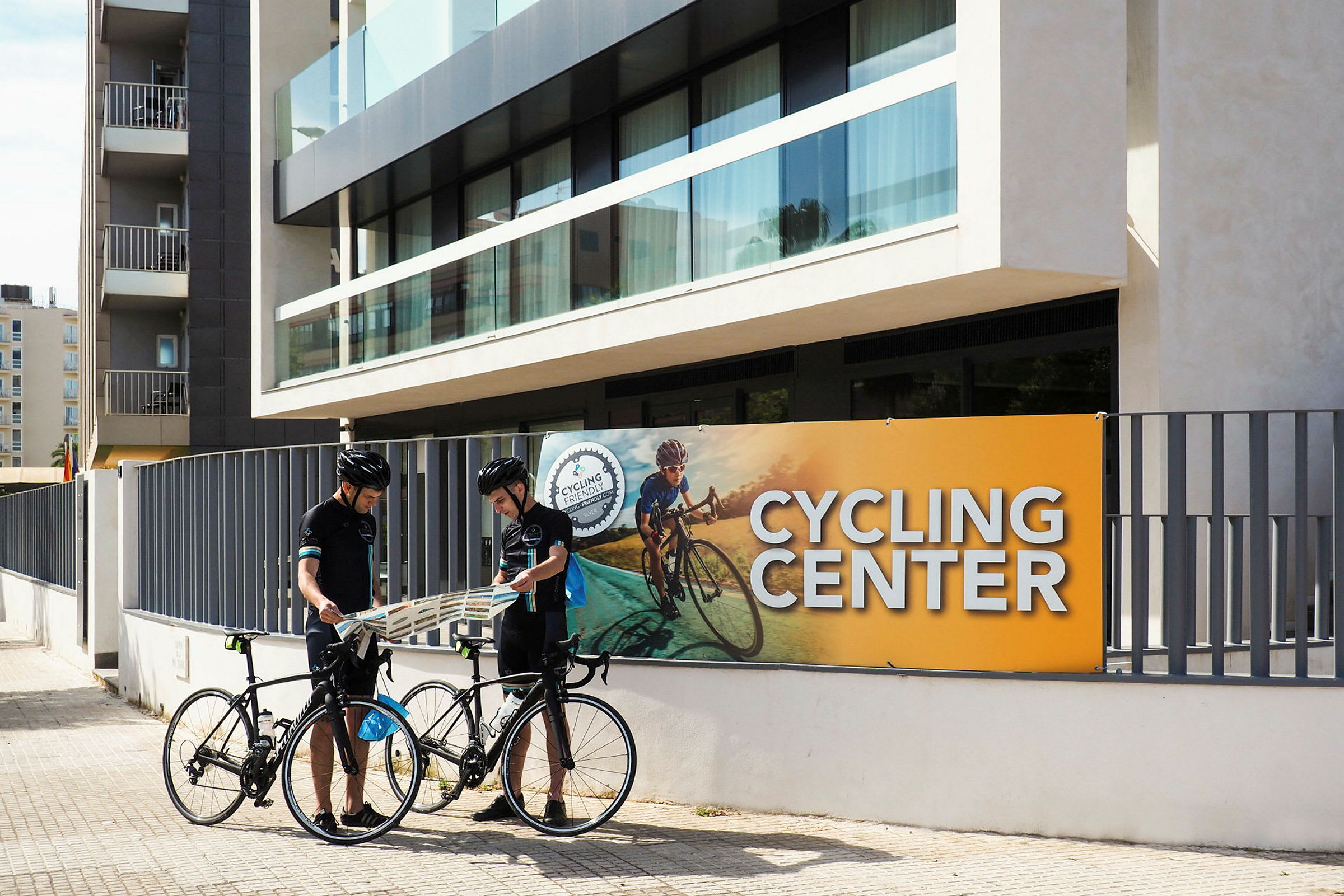 Två personer står med sina cyklar framför en byggnad markerad som Cycling Center. (AI-genererad text)