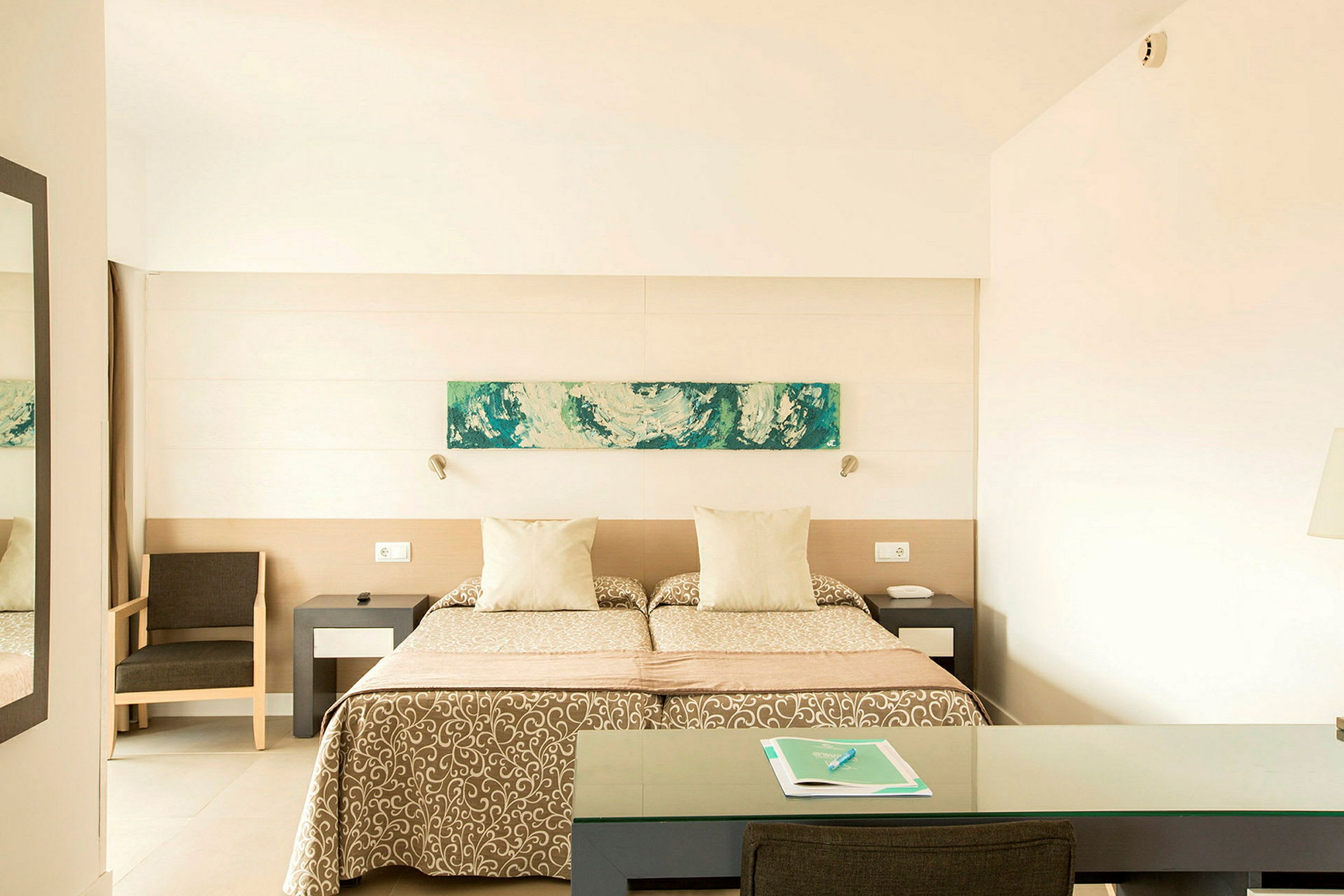 Ett hotellrum med två enkelsängar, en dekoration ovanför sängen, en stol och ett skrivbord. (AI-genererad text)