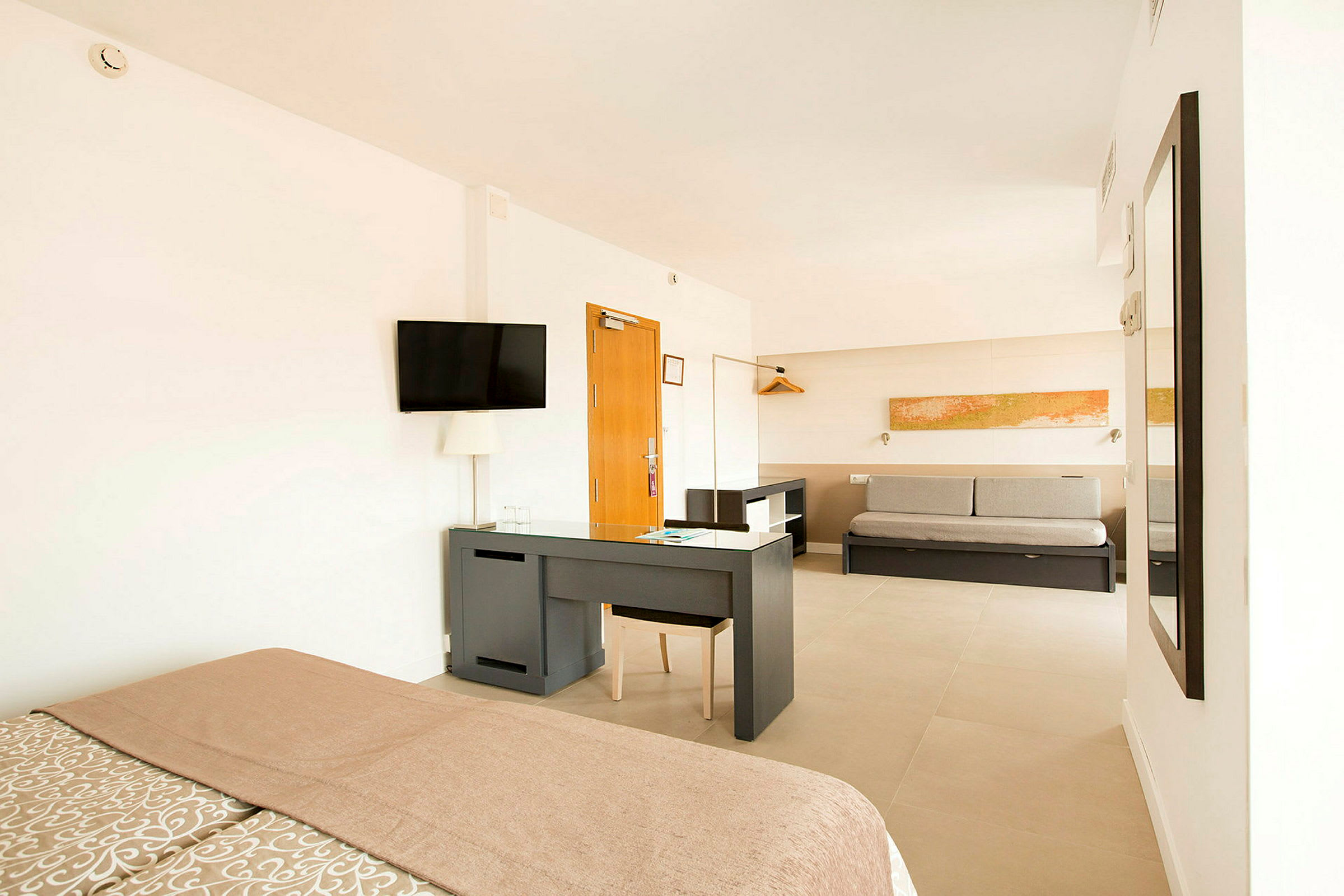 Bild på ett ljust hotellrum med säng, skrivbord, soffa och väggdekor. (AI-genererad text)