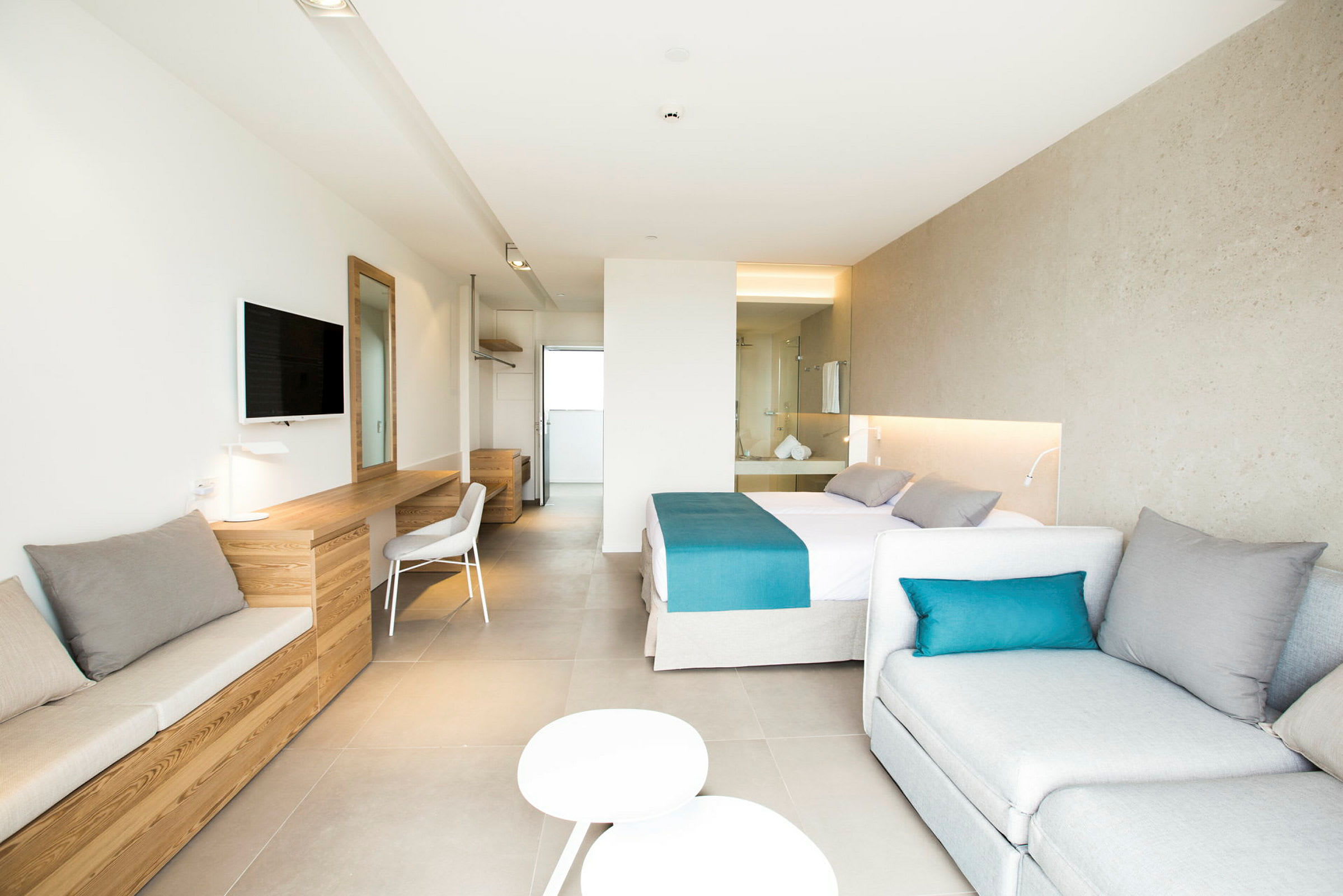 Ett ljust hotellrum med en dubbelbädd, sittmöbler, skrivbord och väggmonterad TV. Rummet har modern inredning och är väl upplyst. (AI-genererad text)