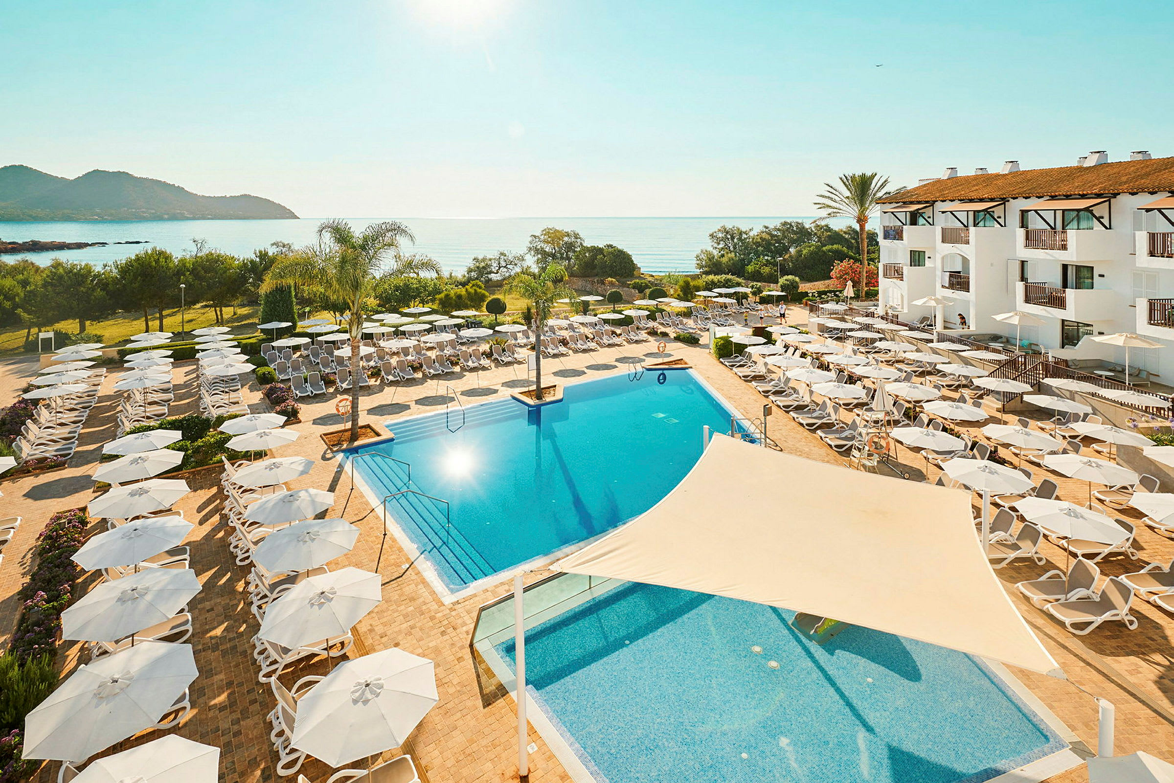 Semesteranläggning med pool, solstolar och parasoller nära havet. (AI-genererad text)