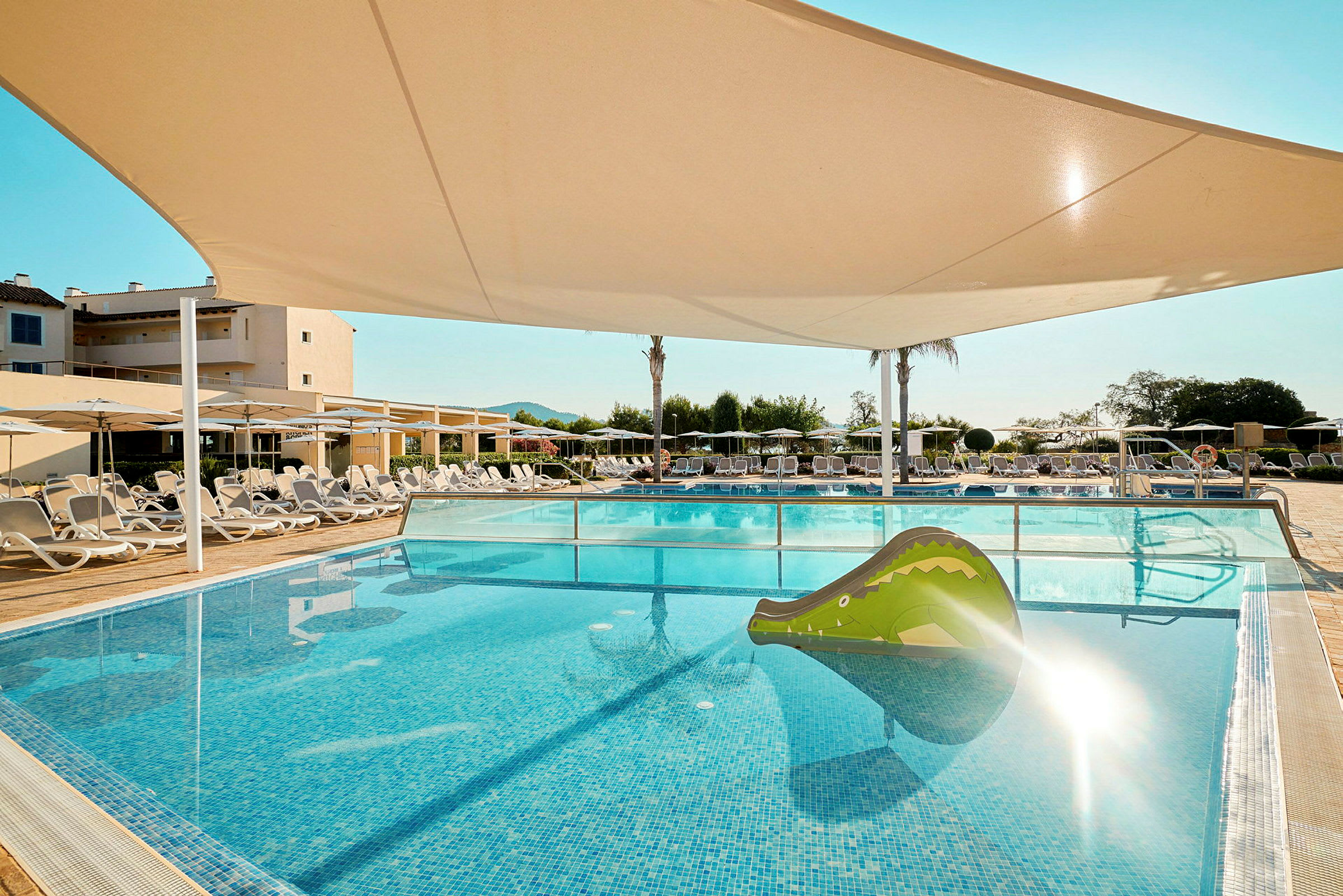 En pool med solstolar och parasoller i bakgrunden, under skuggande tak. (AI-genererad text)