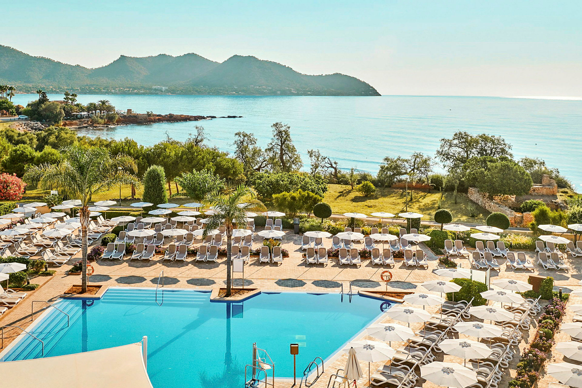 Hotellpool med solstolar och parasoll, utsikt mot havet och berg. (AI-genererad text)