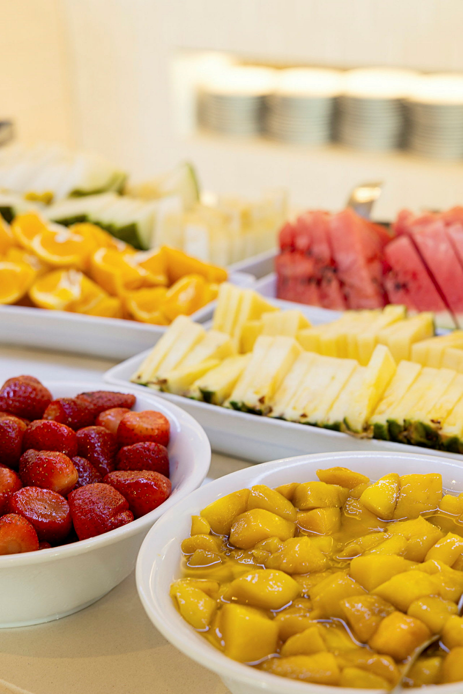 Uppskuren frukt, inklusive jordgubbar, mango, melon och ananas, serverad i vita skålar. (AI-genererad text)