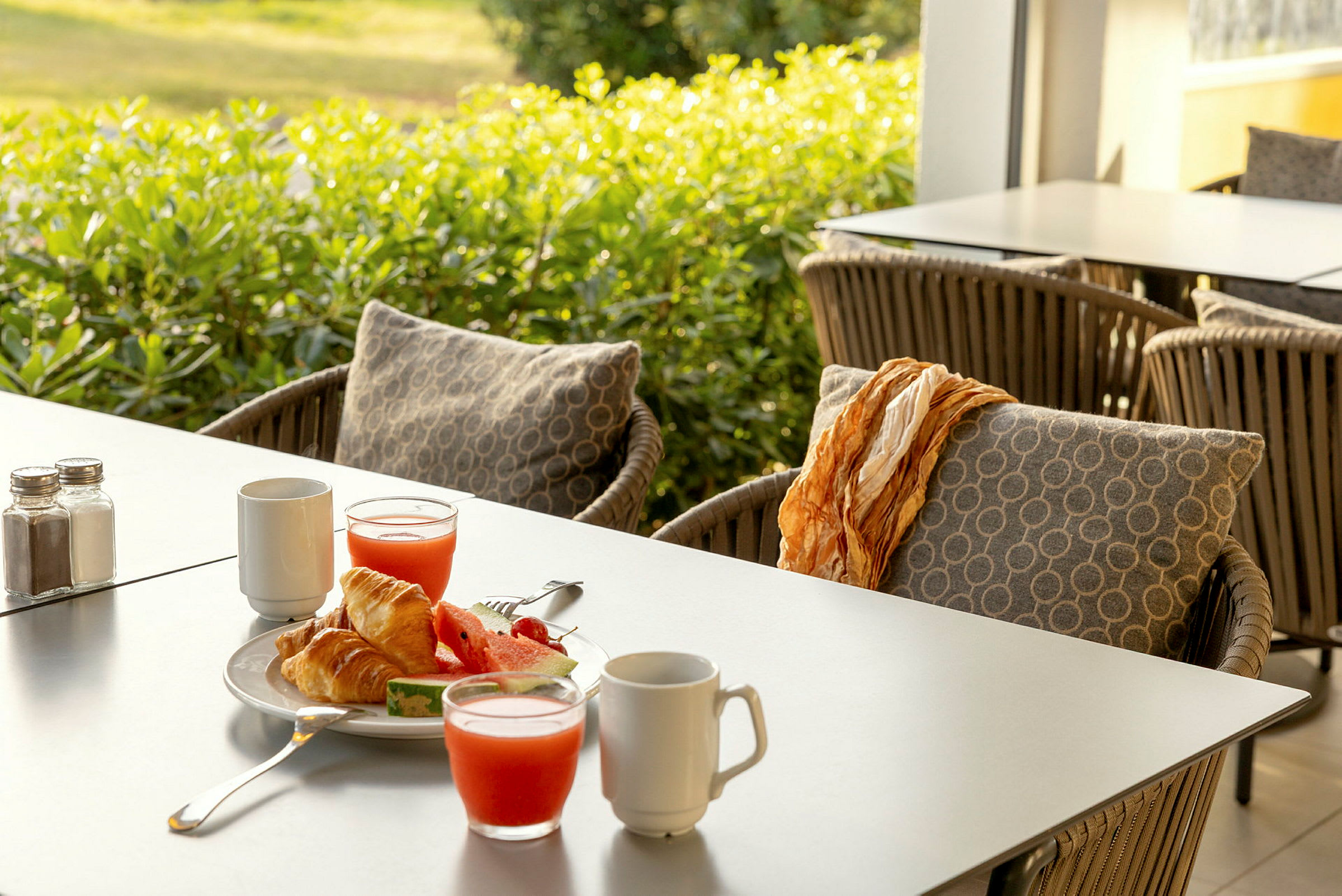 Frukost med croissanter, vattenmelon och juice på ett bord med utemöbler. (AI-genererad text)