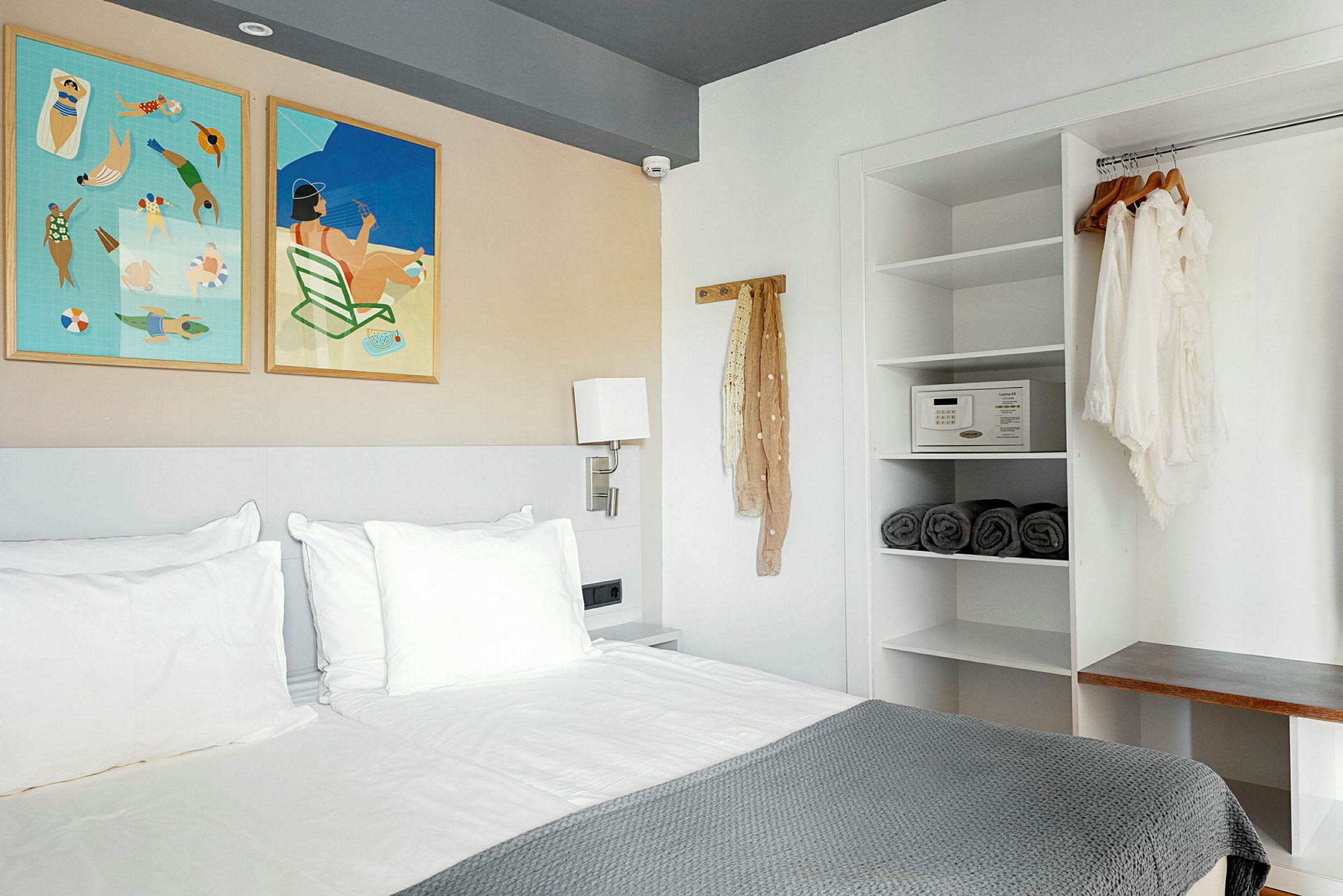 Ett modernt hotellrum med en säng, vägghängda tavlor och en öppen garderob. (AI-genererad text)