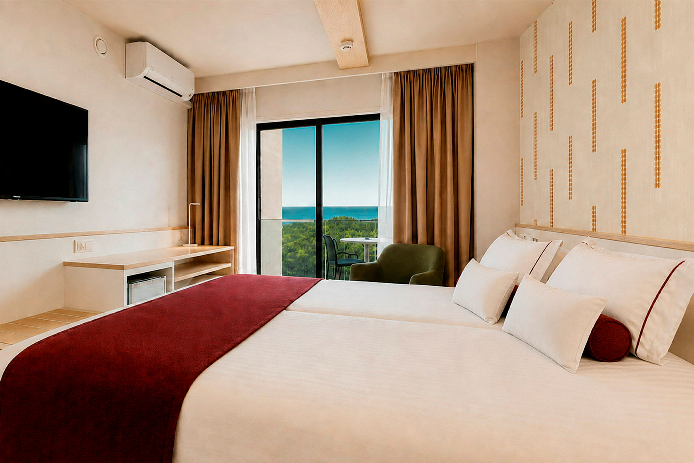 Ett hotellrum med två sängar, röda täcken, en TV på väggen och utsikt mot havet genom fönstret. (AI-genererad text)