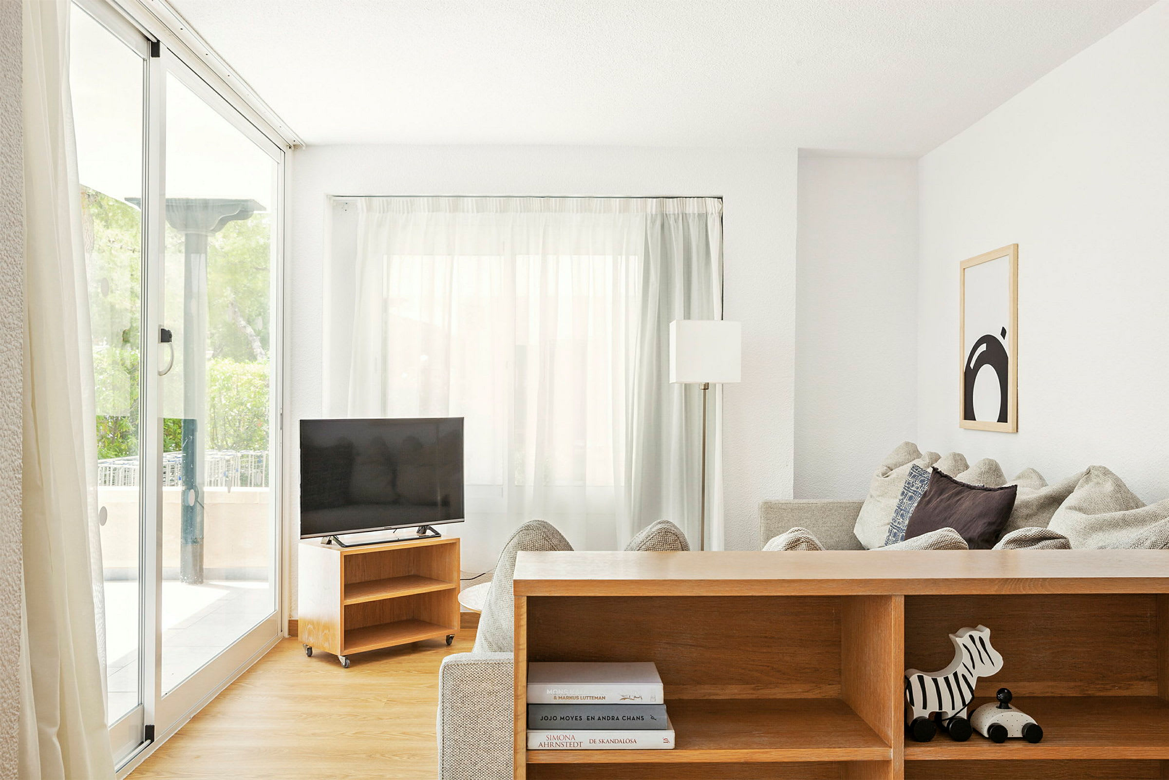 Vardagsrum med stora fönster, soffa, TV och en bokhylla. (AI-genererad text)