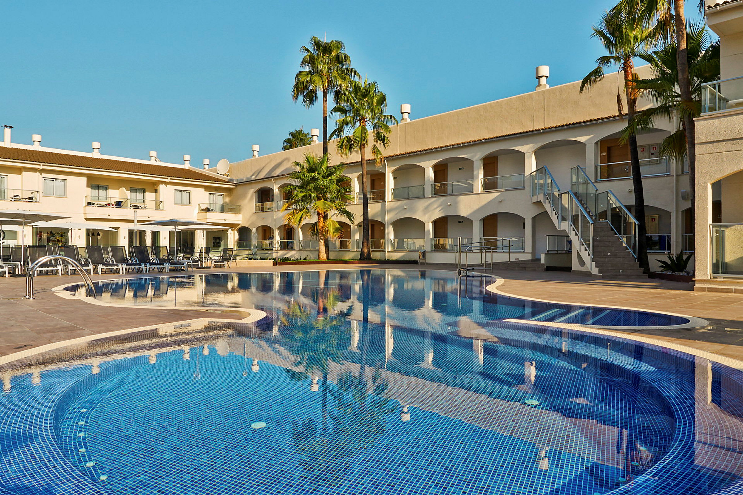 Bild av en hotellpool med solstolar och byggnader i bakgrunden. (AI-genererad text)