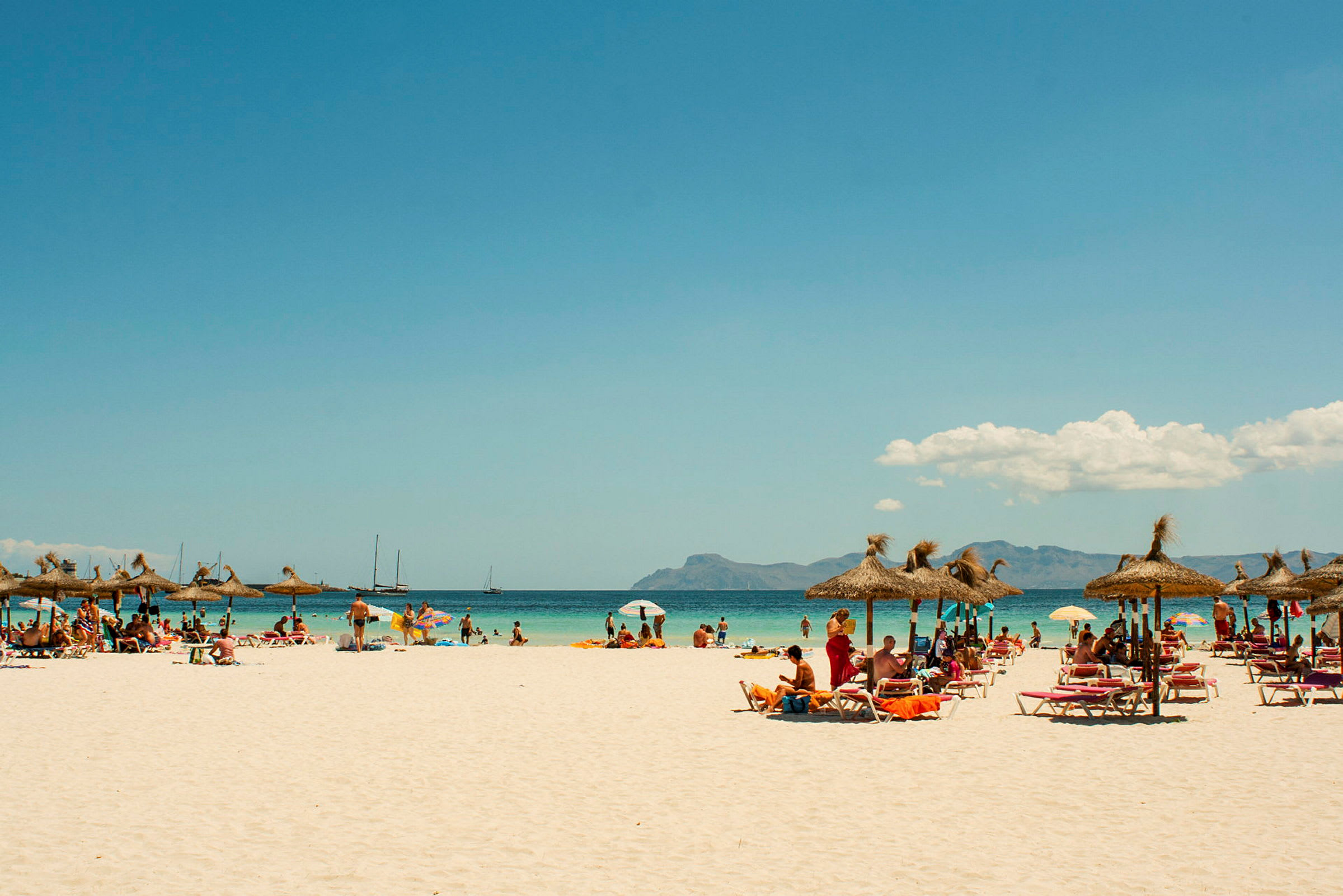 Strand med parasoller och solstolar, människor badar och njuter av solen. (AI-genererad text)