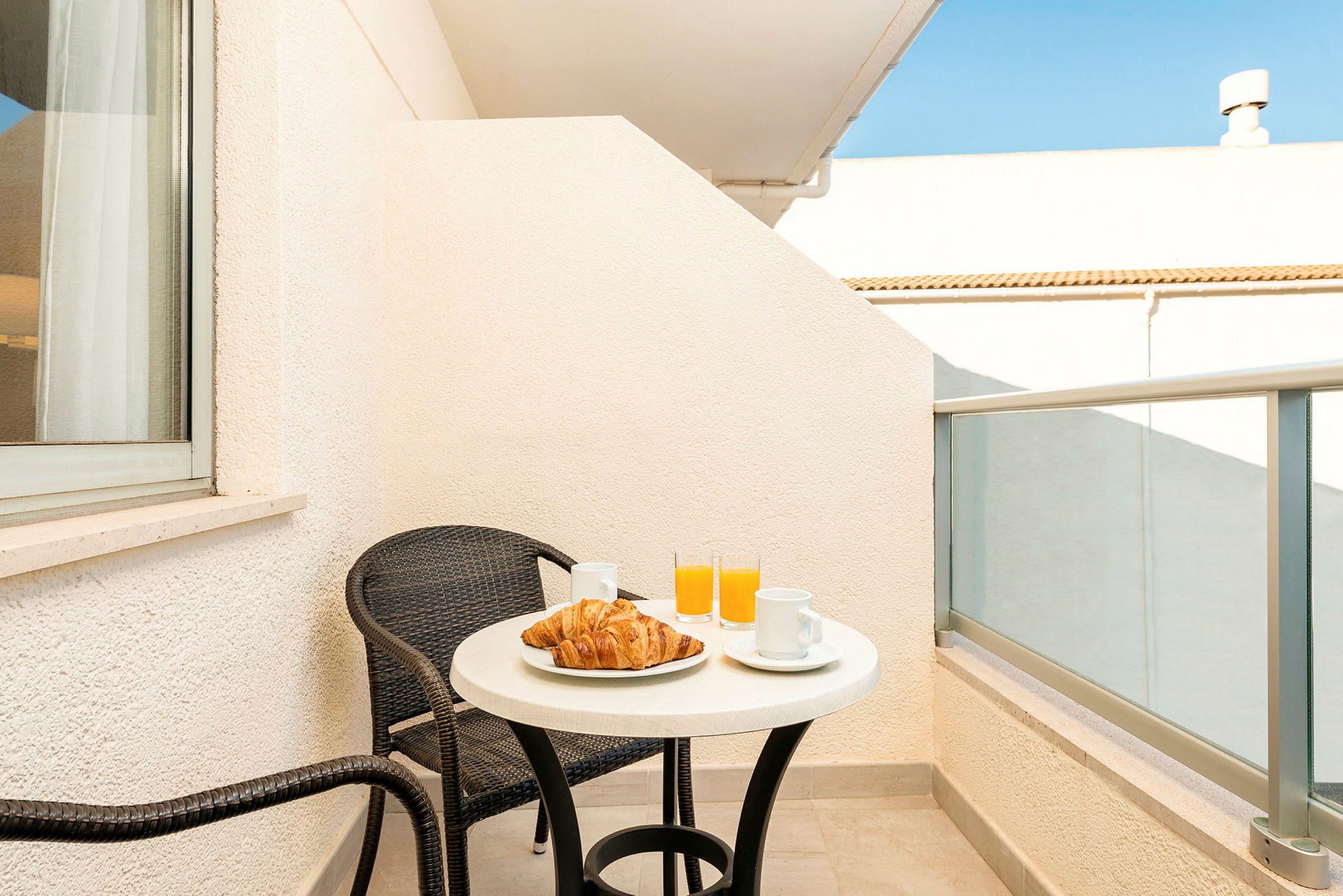 En balkong med ett bord, två stolar, croissanter, kaffekoppar och glas med apelsinjuice. (AI-genererad text)