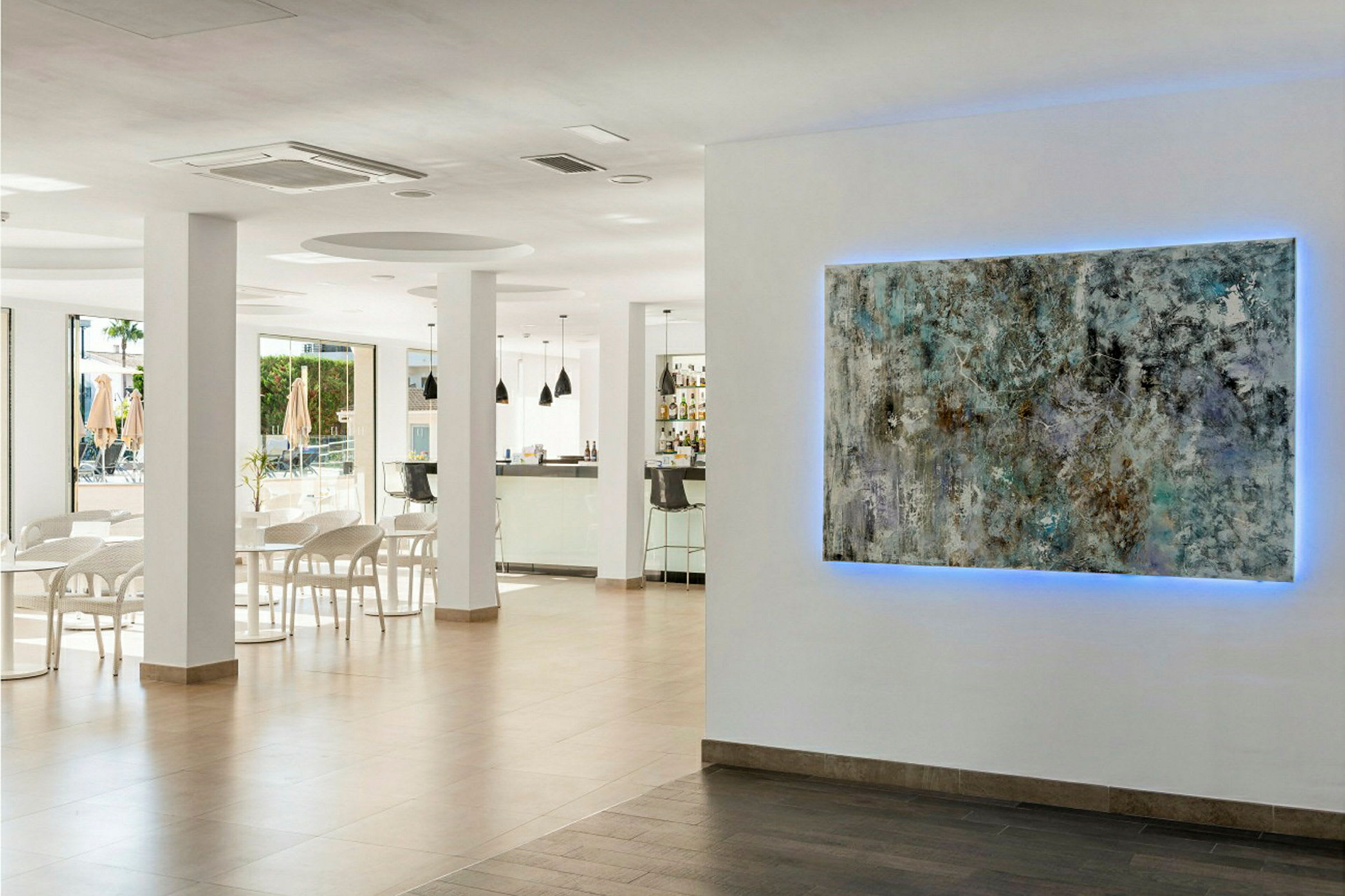 Interiör av ett modernt caféområde. På väggen hänger ett konstverk med blått ljus bakom. (AI-genererad text)
