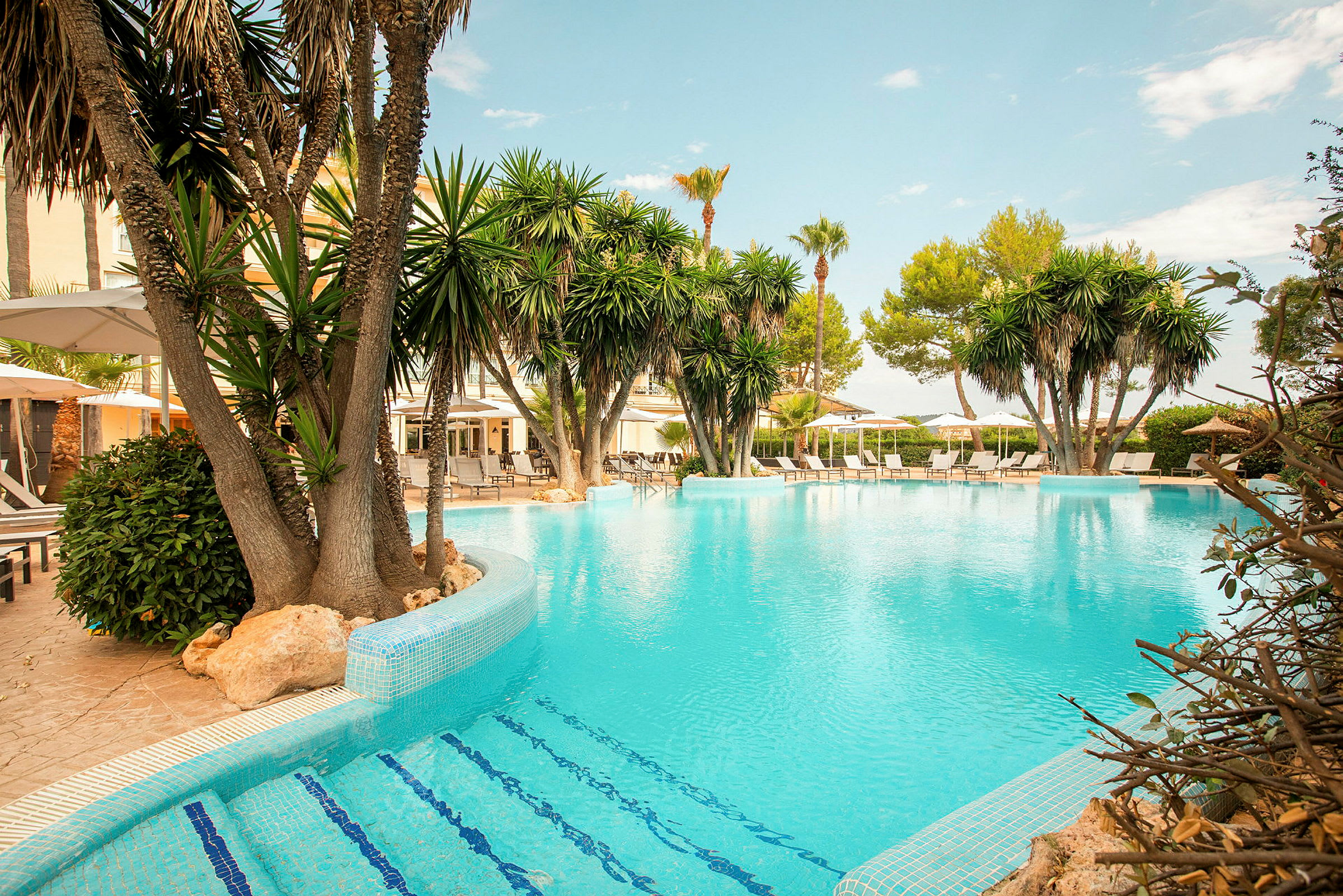 En pool omgiven av palmer och solstolar vid en hotellanläggning. (AI-genererad text)