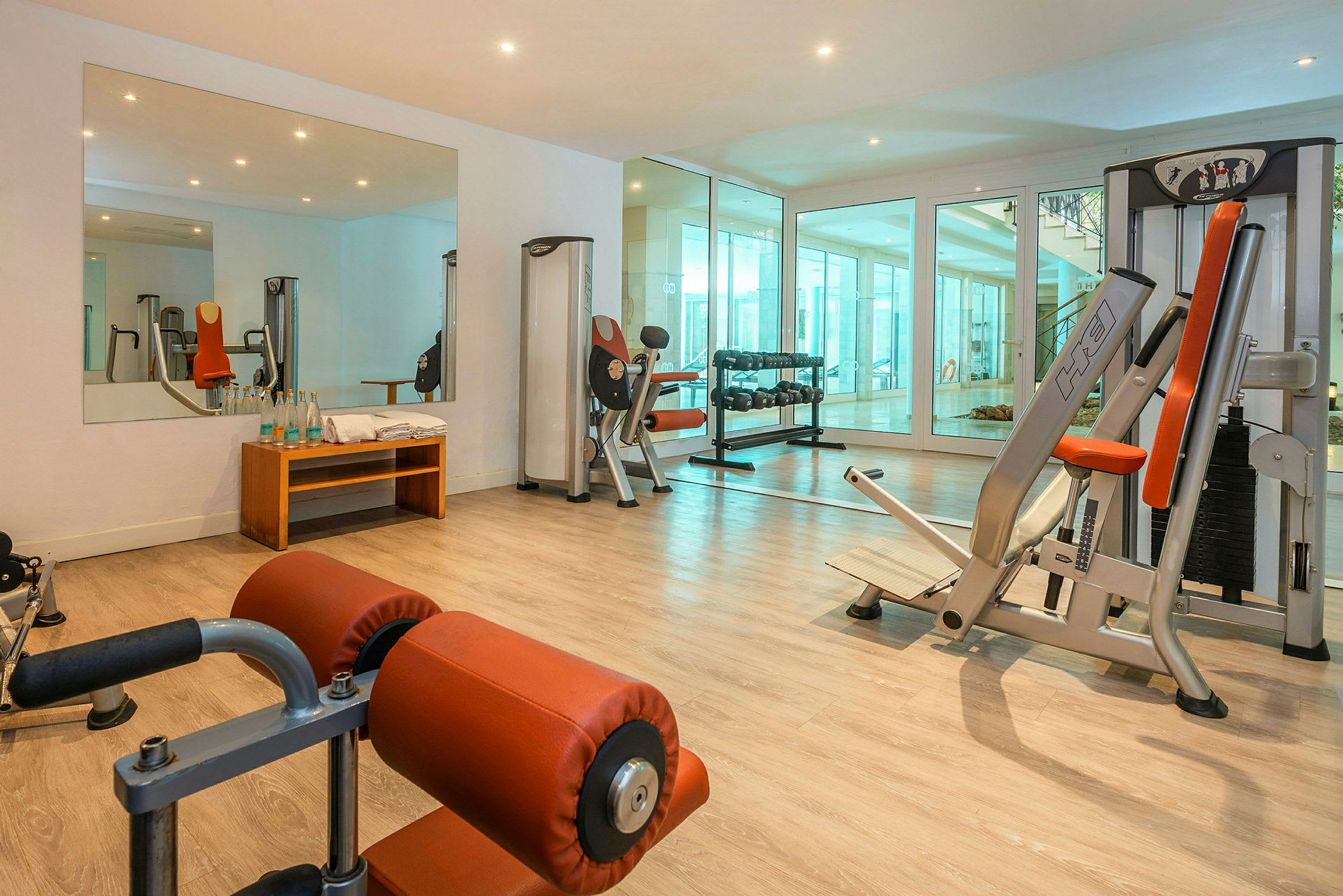 Ett gym med träningsmaskiner, spegel, hantlar och en bänk. (AI-genererad text)