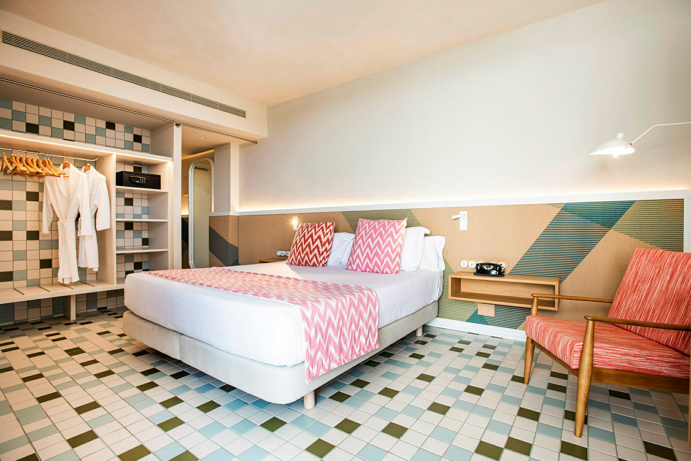 Hotellrum med dubbelsäng, färgglada kuddar, och sittplats vid sidan. (AI-genererad text)
