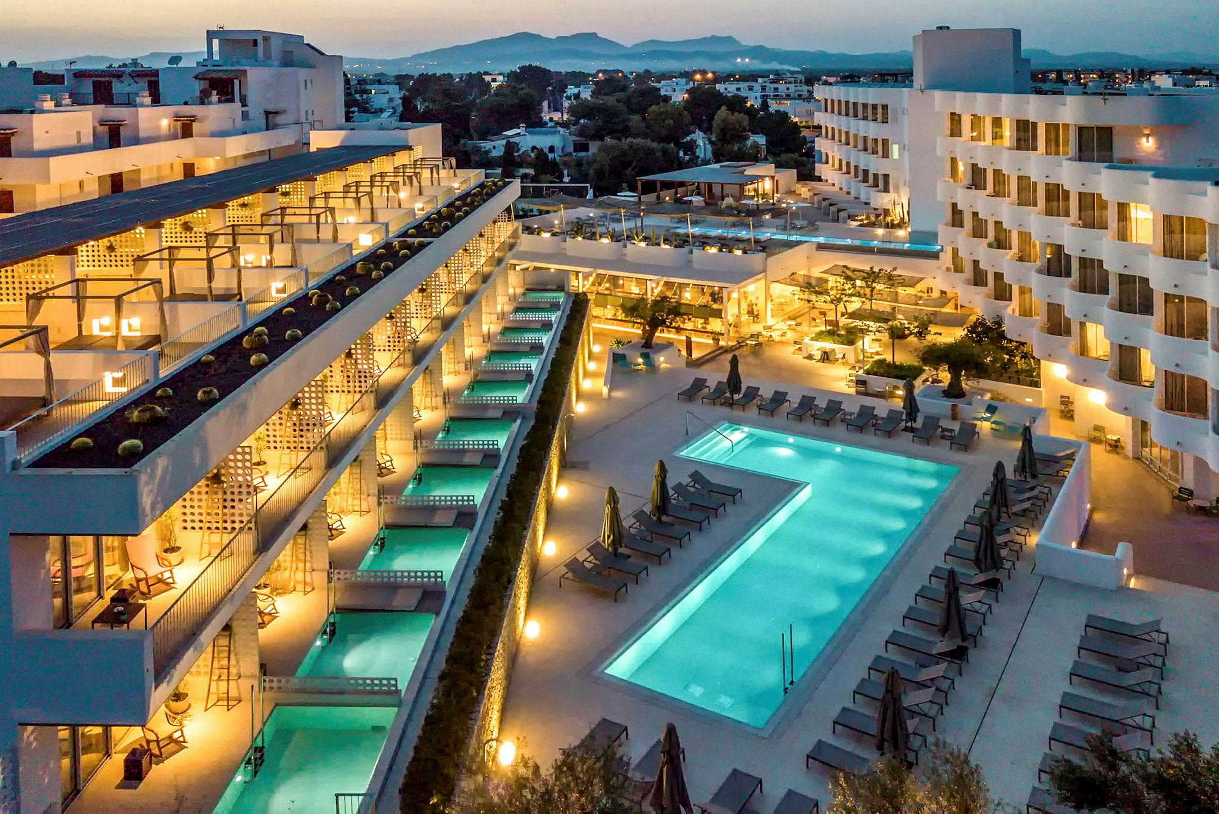 Hotellområde med byggnader, pooler och solstolar vid kvällstid. (AI-genererad text)