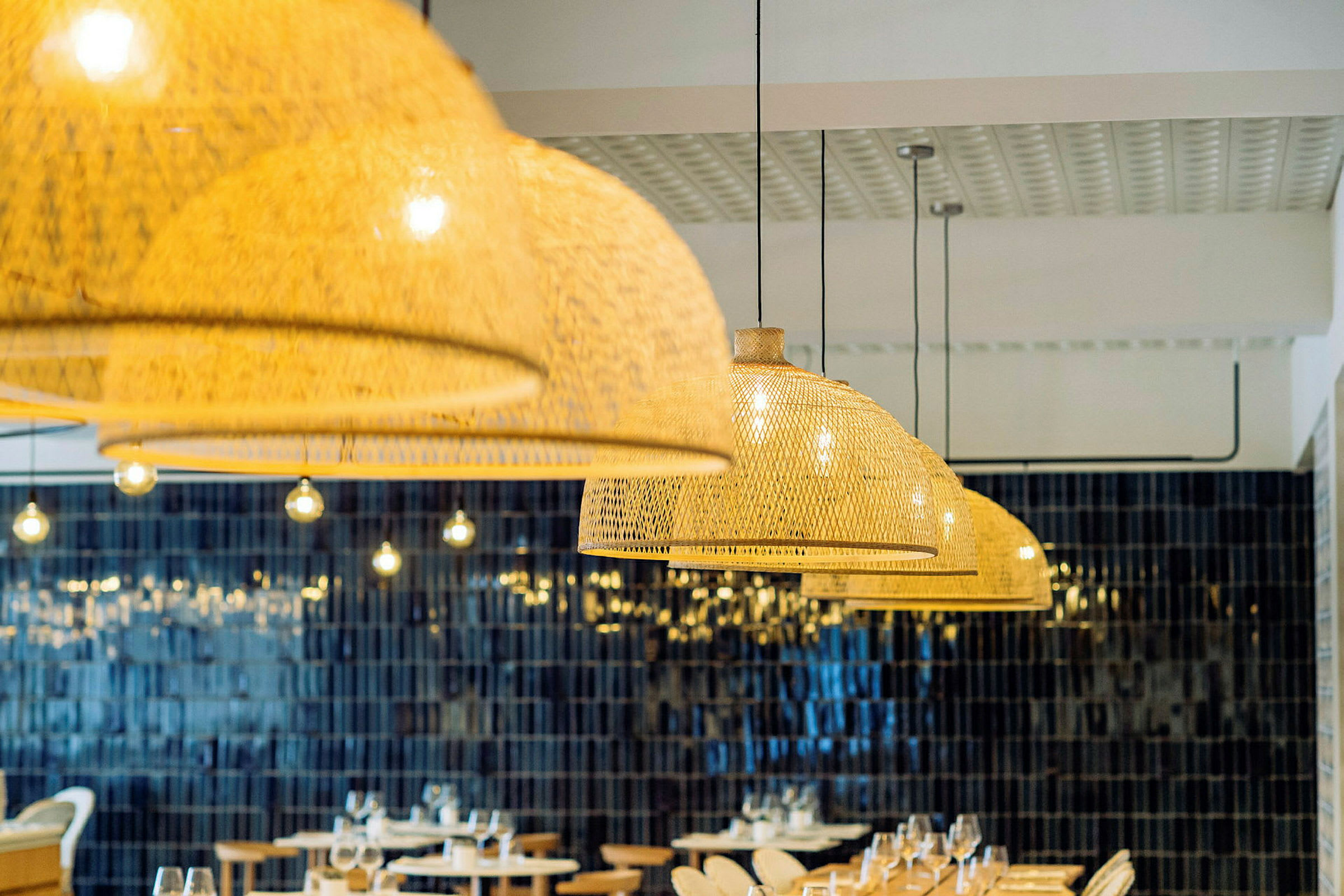 Restauranginteriör med hängande flätade lampskärmar och bord med dukning. (AI-genererad text)
