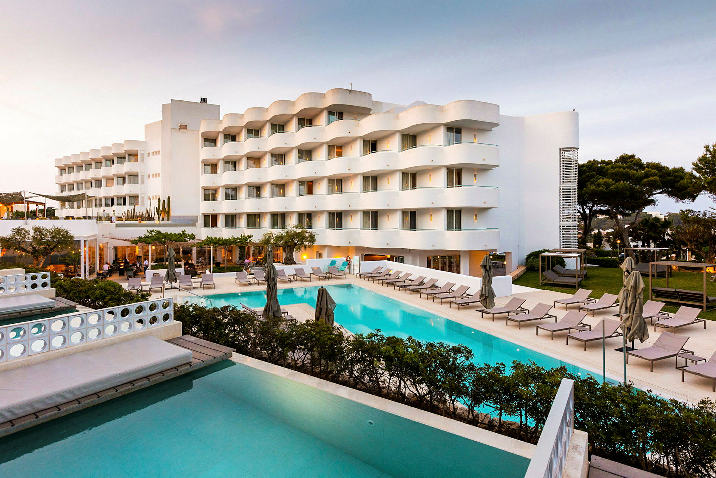 Bild av ett hotell med poolområde och solstolar, omgivet av gröna träd och vegetationen. (AI-genererad text)