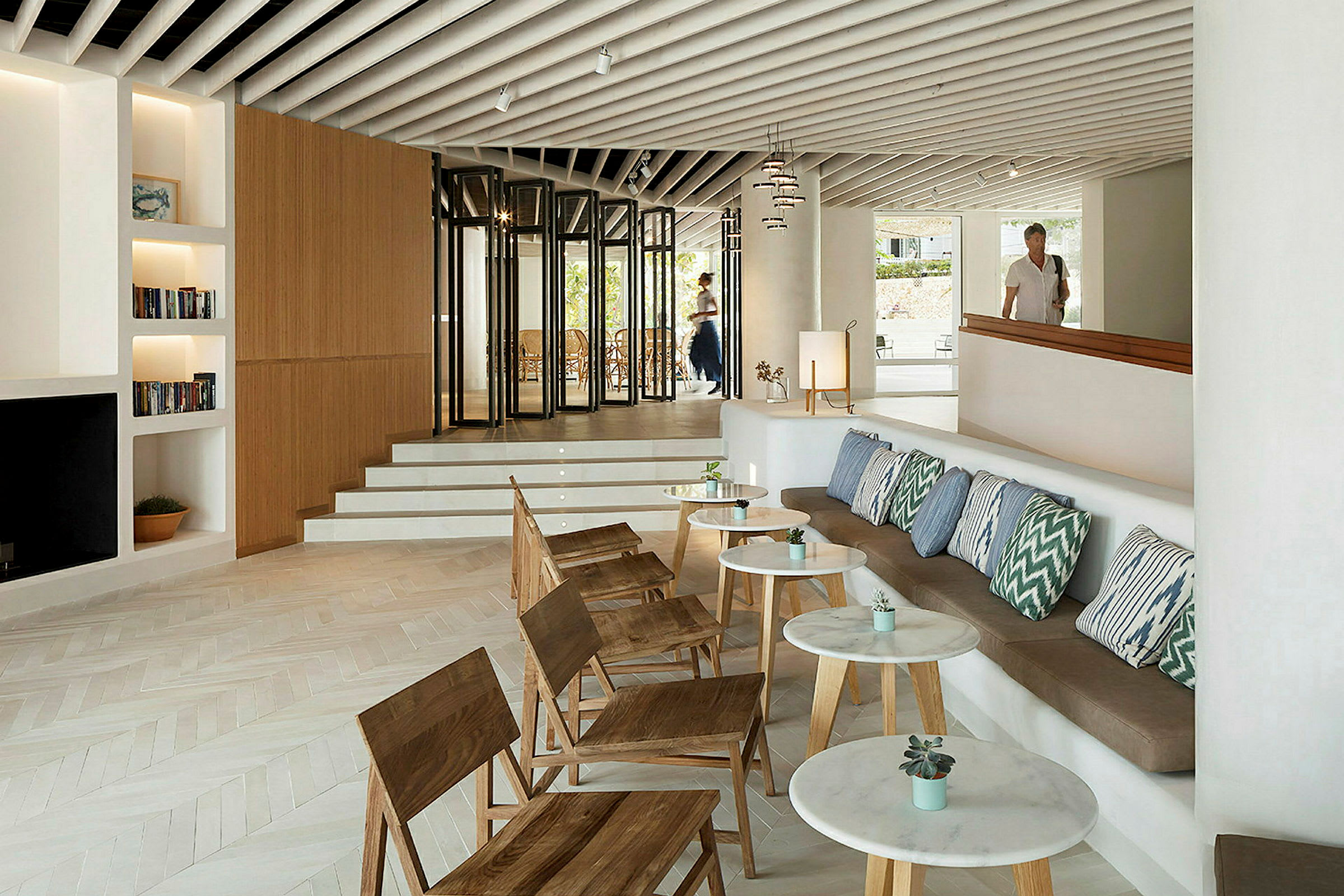Ett modernt hotellrum med sittgrupp, trästolar, kuddar och små bord. (AI-genererad text)