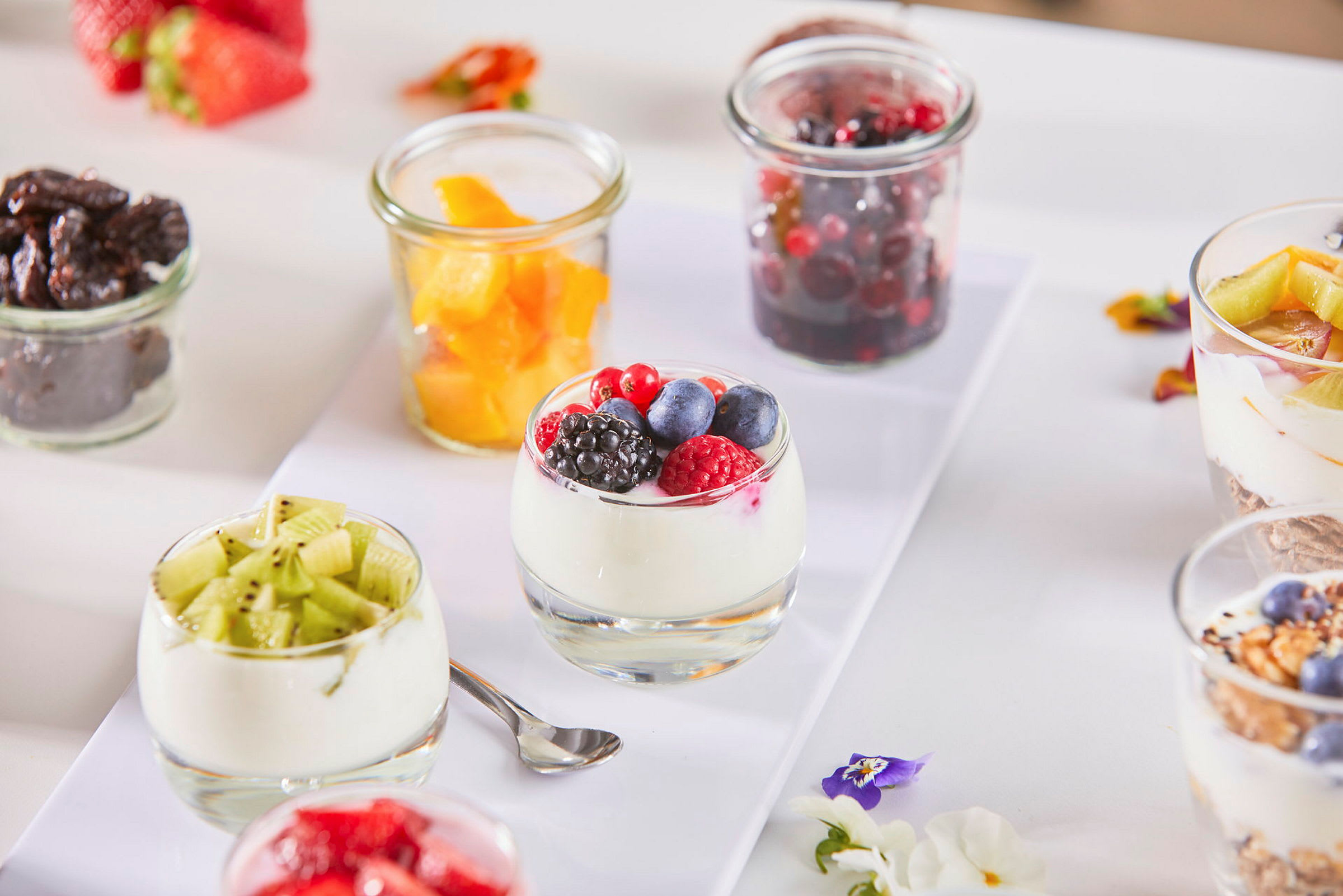 Glas på ett bord med yoghurt dekorerad med olika frukter och bär. (AI-genererad text)