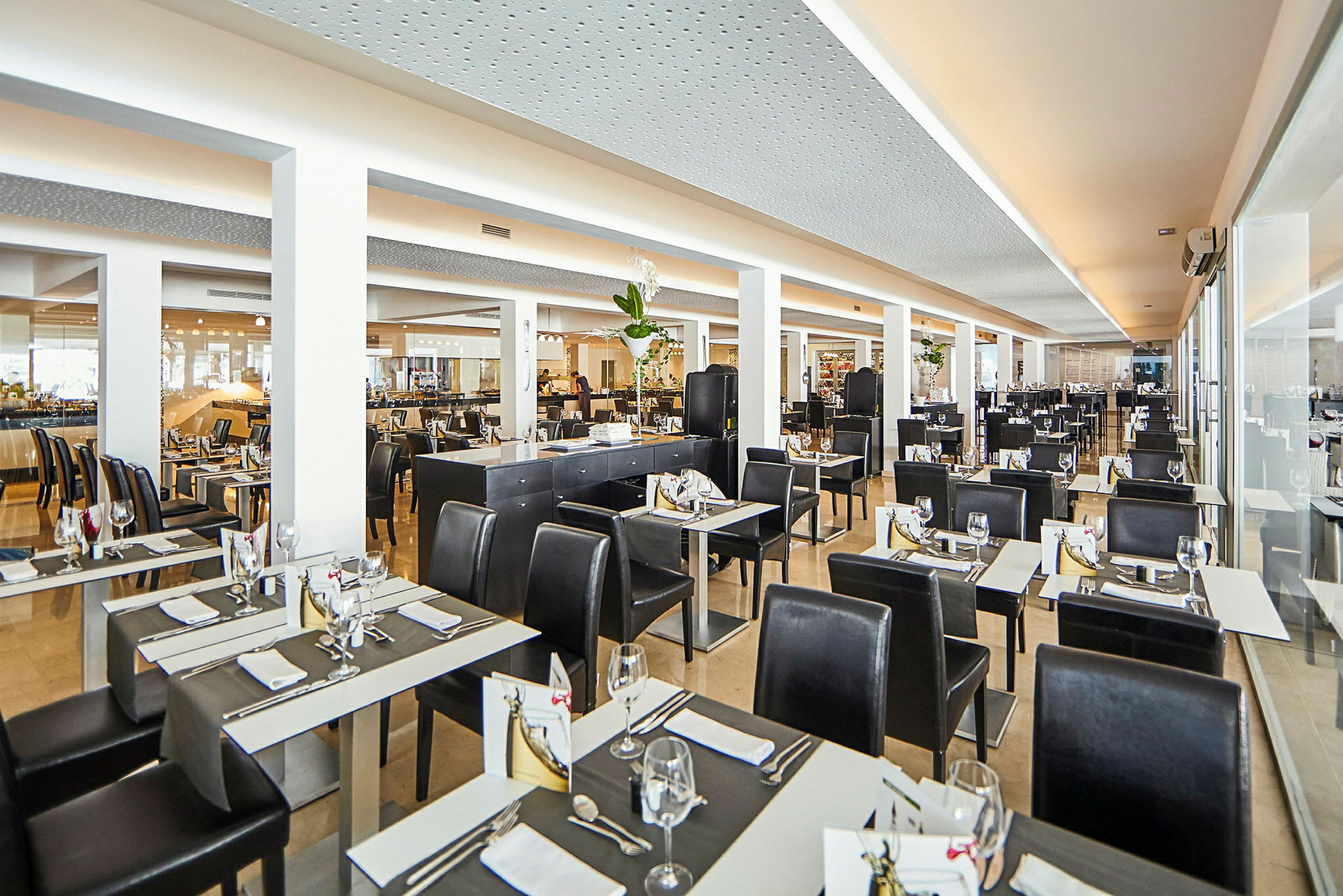 Ett ljust och modernt restaurangområde med dukade bord och svarta stolar. (AI-genererad text)