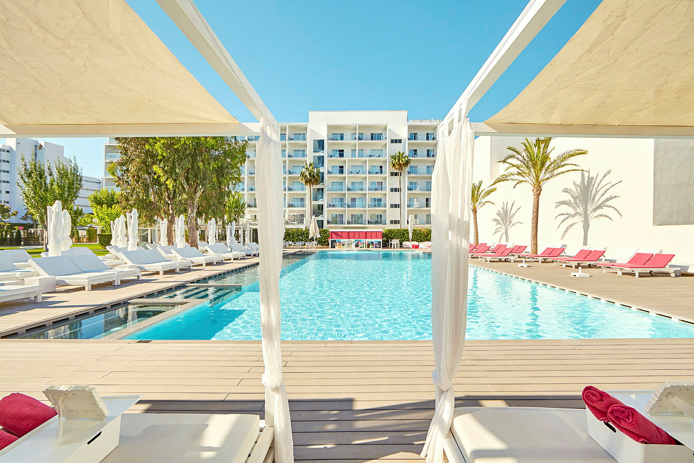 Bild på en pool framför ett modernt hotell, med solstolar och palmer runtom. (AI-genererad text)